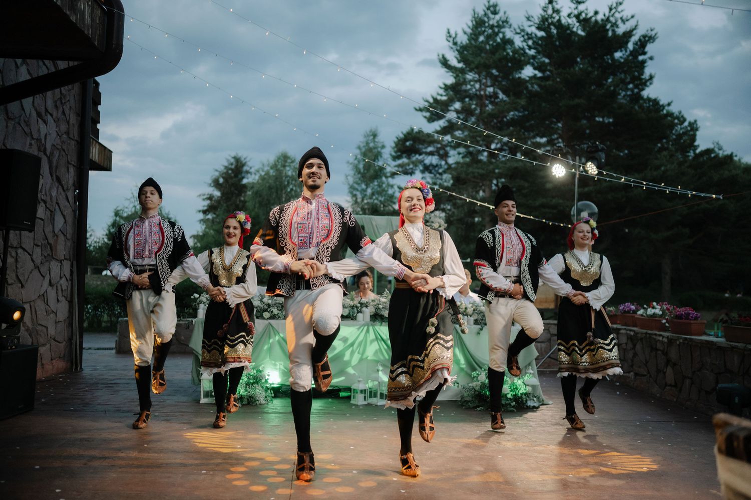 Wedding party members leap and dance together in a joyful celebration at dusk with dramatic lighting and smoke effects.