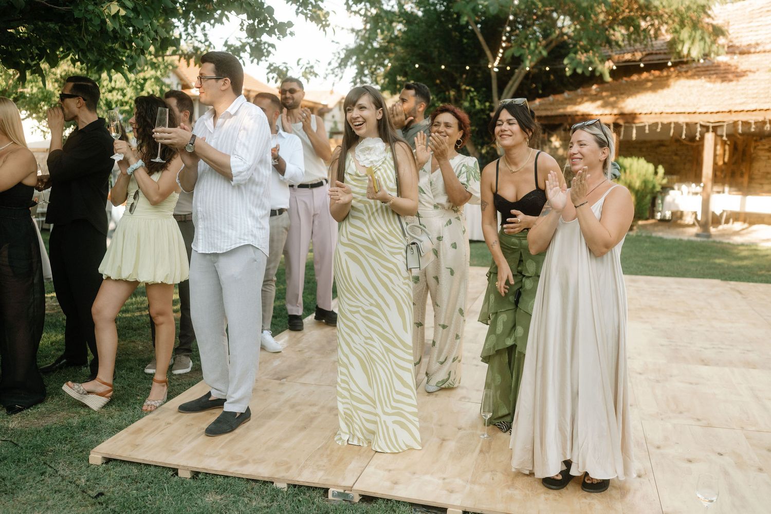 Wedding guests stand on a wooden platform outdoors during an emotional ceremony moment at a garden reception.