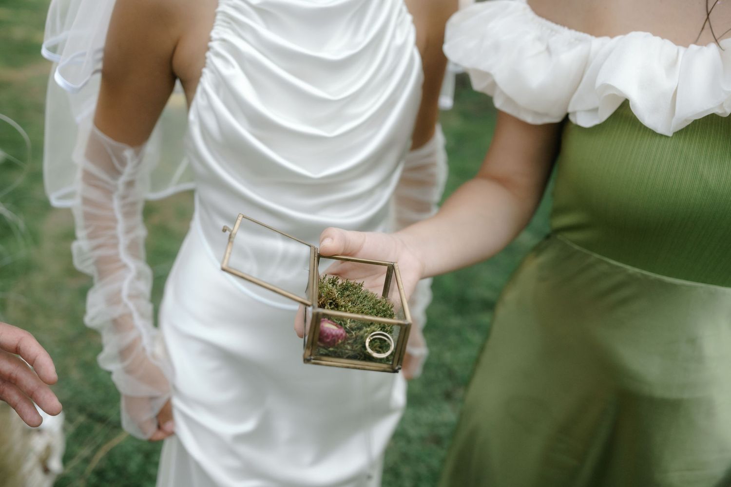 Hands holding a small gold camera against a backdrop of white and green formal attire.