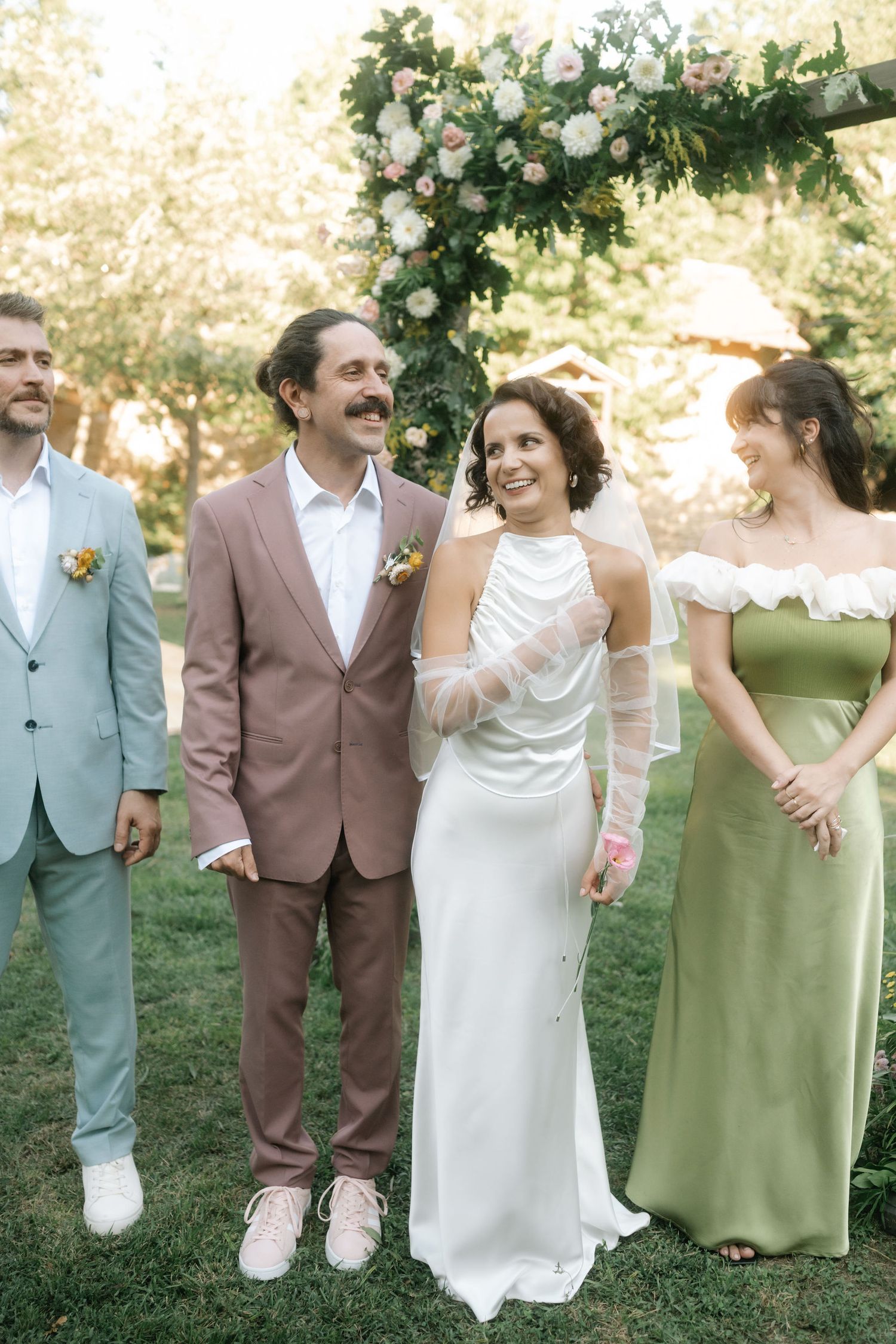 Wedding group in coordinated sage green and brown outfits laughing together during outdoor photo session.