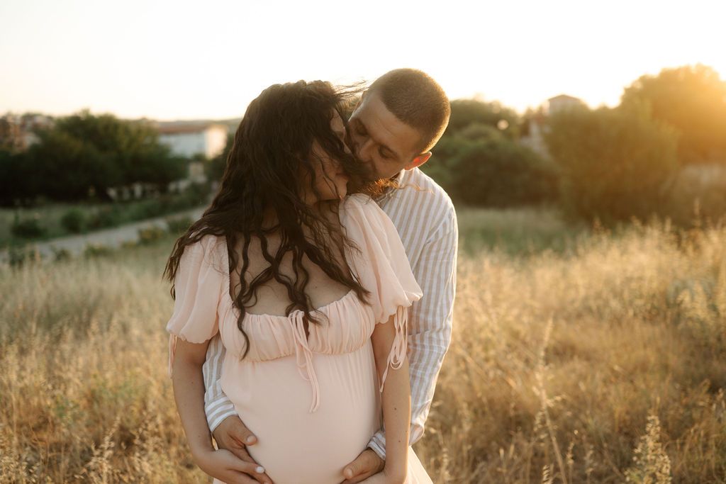 A couple embraces in a sunlit field of tall grass during golden hour at sunset.