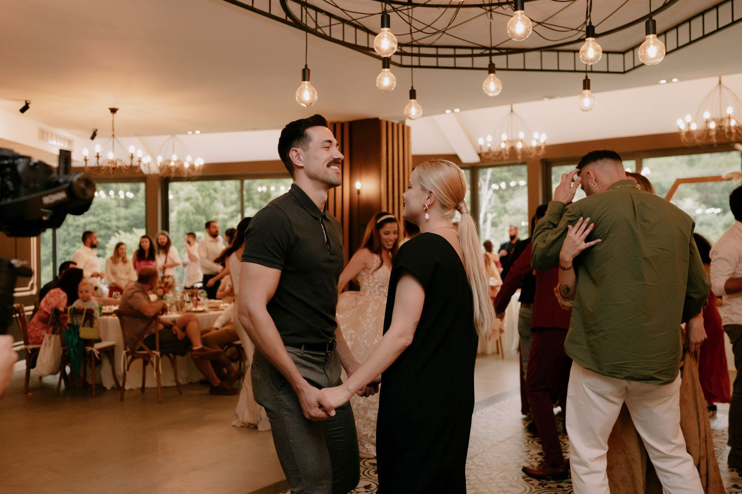 Couples dance together on a rustic wooden dance floor at a wedding reception with string lights overhead.