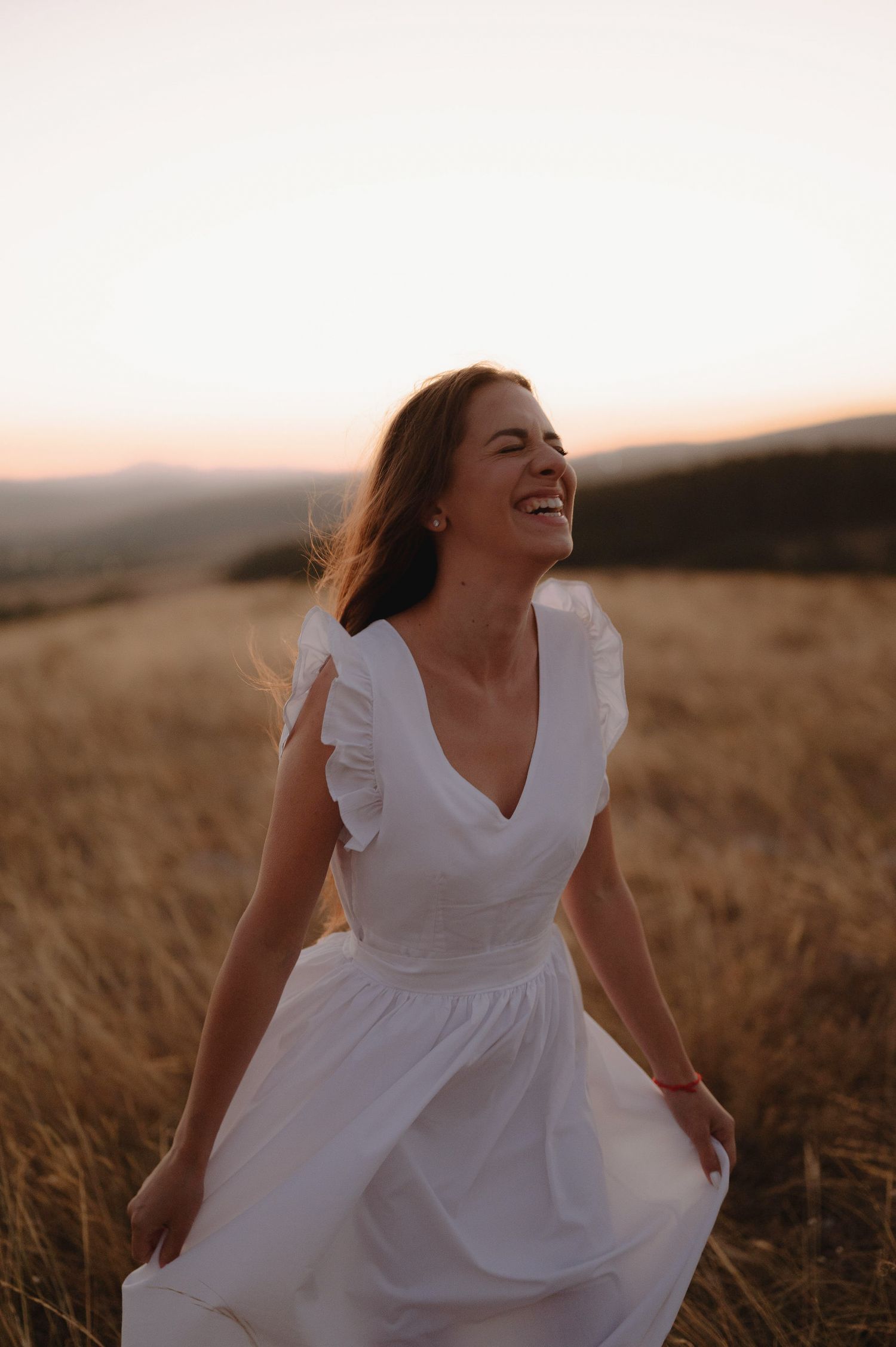 Woman in flowing white dress twirling joyfully in a golden wheat field at sunset.