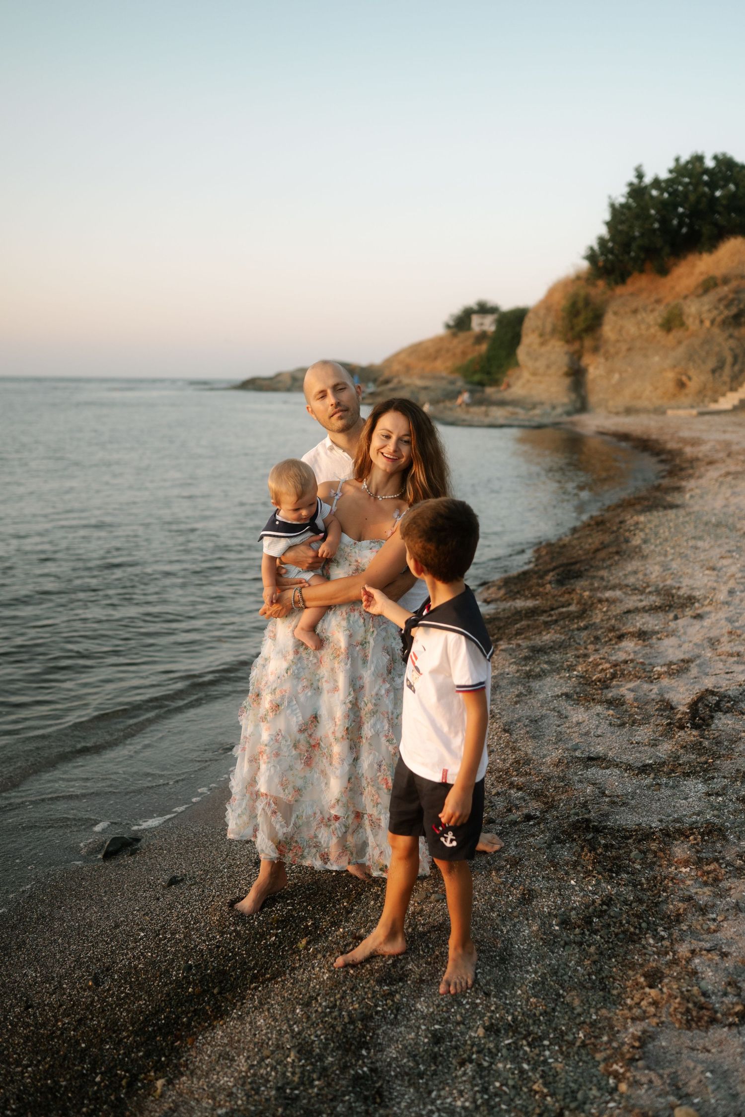 Children play together on a rocky beach at sunset near coastal cliffs and calm waters.
