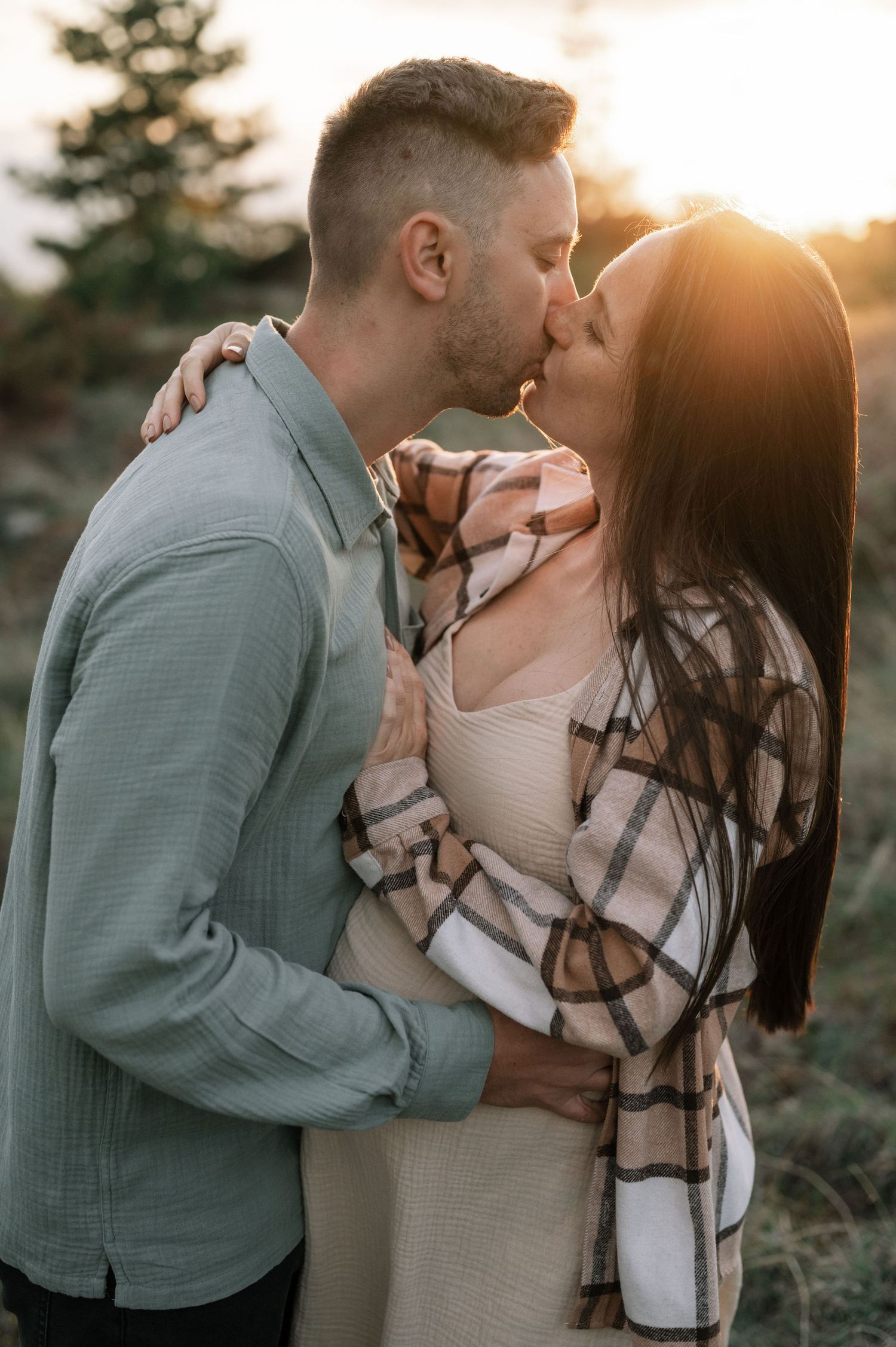 Romantic couple embracing in a sunset-lit outdoor setting with trees in the background.