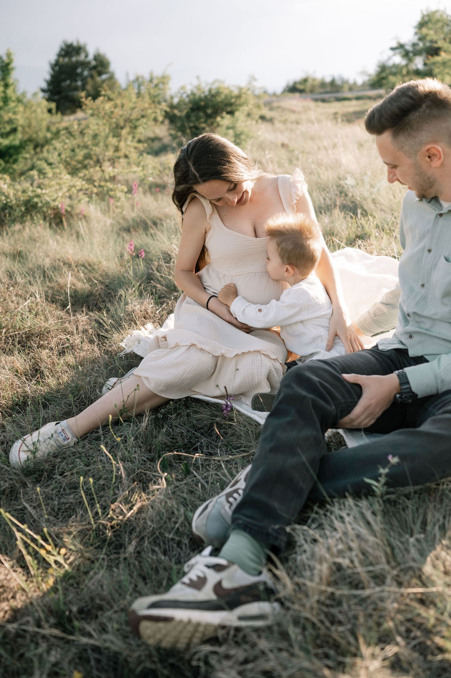 Family enjoying a tender moment together while sitting on a grassy hillside at sunset.