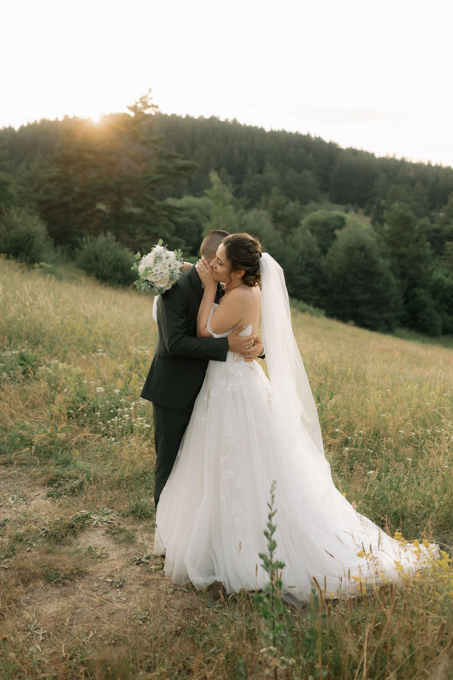 Newlywed couple shares romantic moments in a sunlit meadow with wildflowers at golden hour.