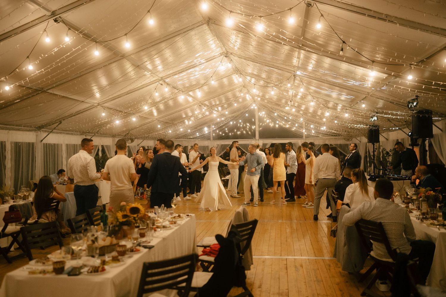 Wedding reception inside an elegant tent venue with string lights overhead and guests dancing on wooden floors.