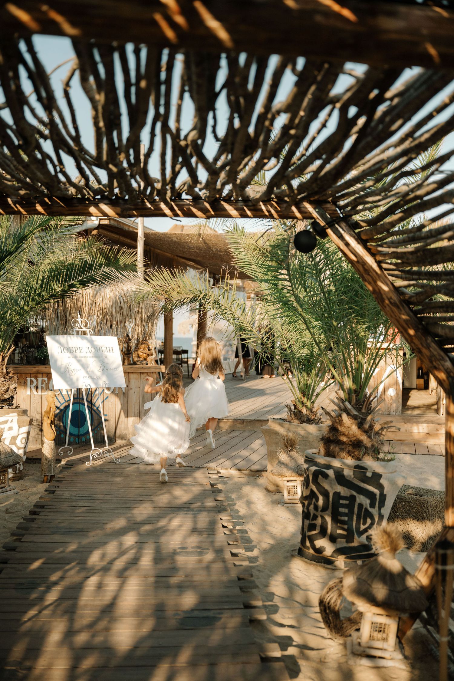Rustic beach venue setup with wooden deck and palm frond roof casting intricate shadow patterns.