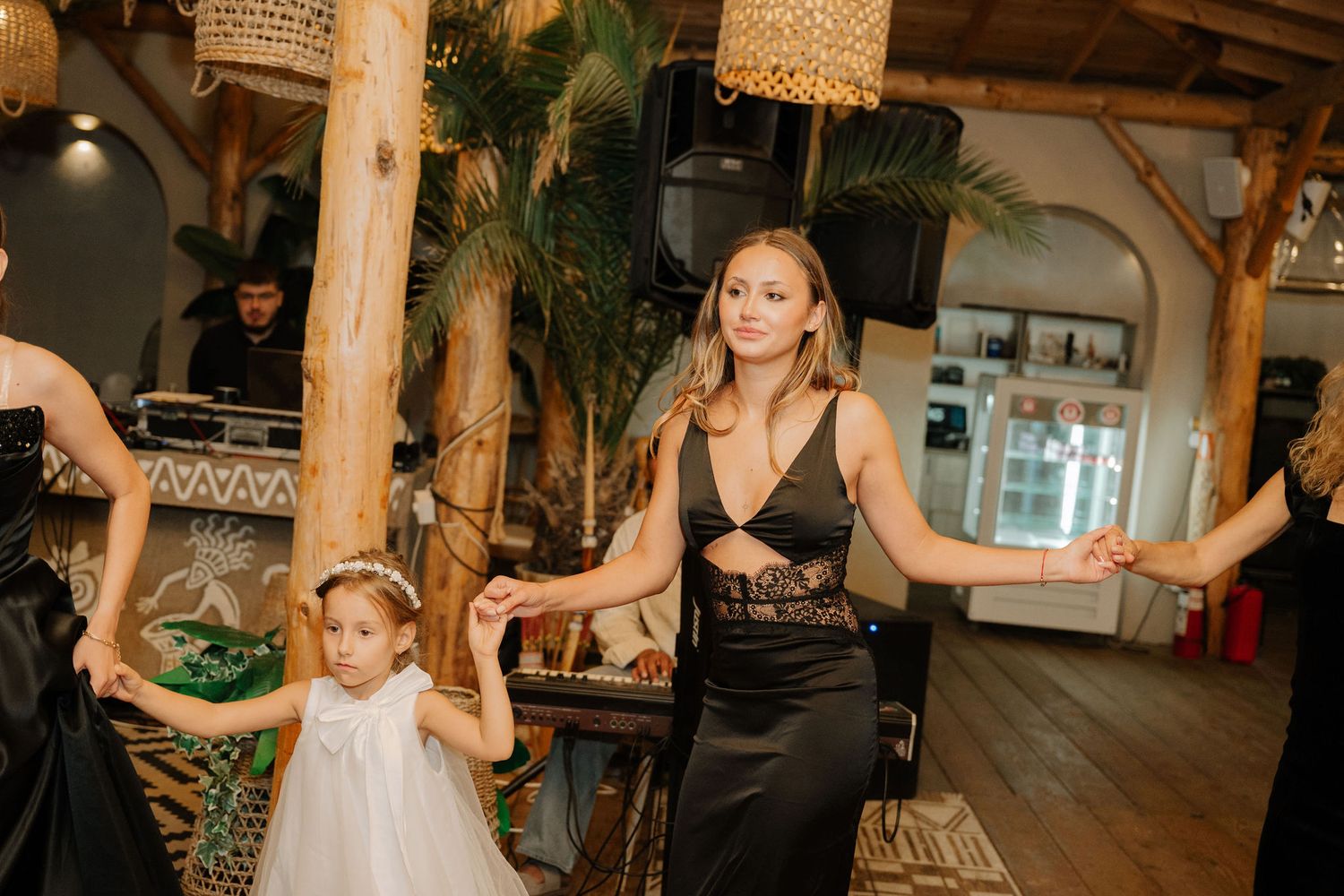 Wedding reception guests dancing and celebrating on a dance floor in an elegant venue with wooden beams and tropical decor.