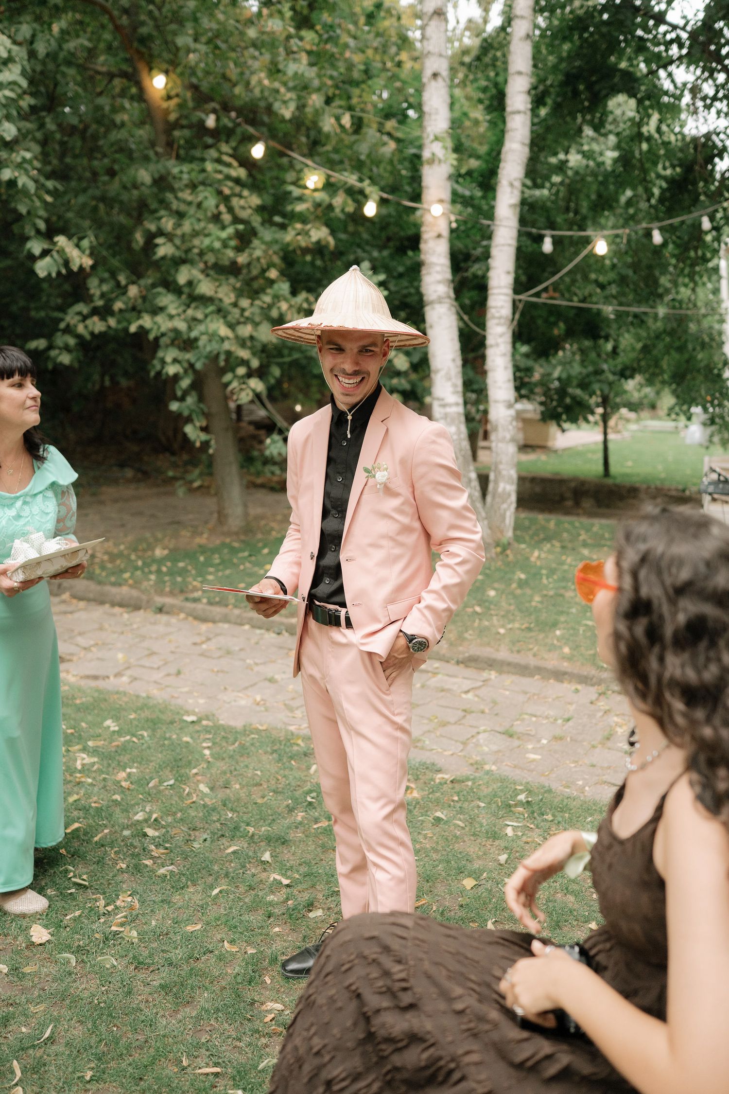 A couple dances together in a wooded outdoor setting with string lights and pink and mint green outfits.