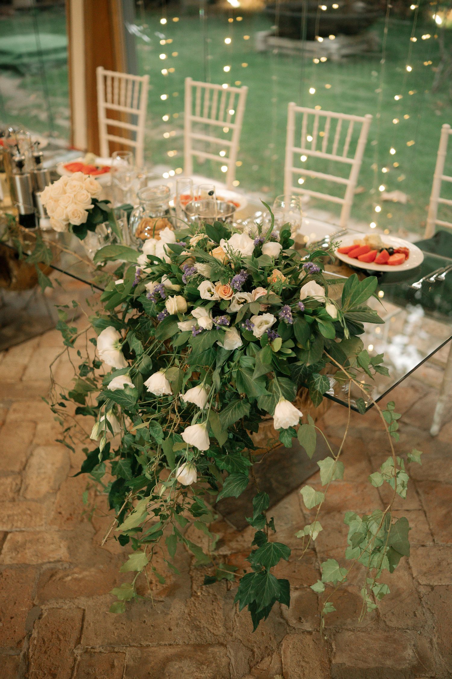 Elegant floral centerpiece with white roses and cascading greenery on a rustic table at a wedding reception.