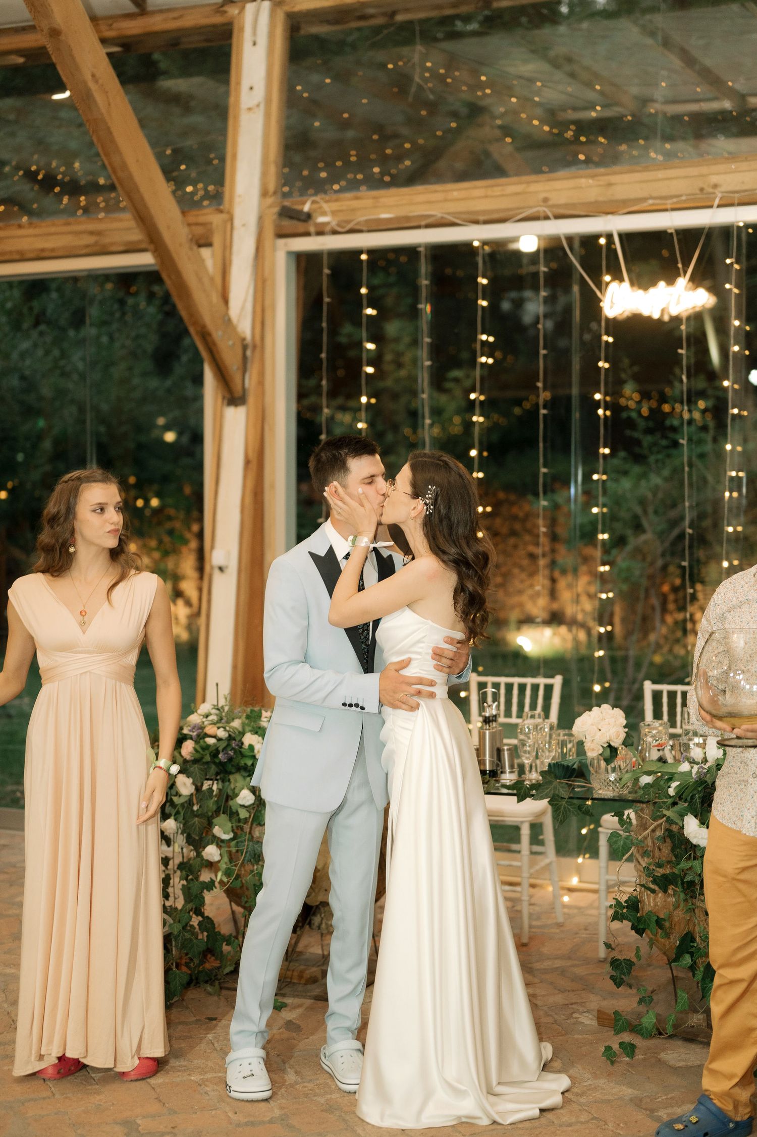 Wedding party dances together in a rustic barn venue decorated with twinkling string lights and floral arrangements.