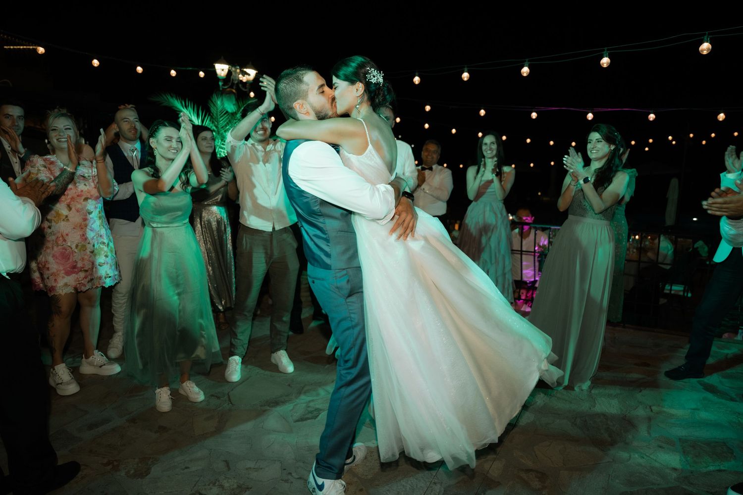 Wedding guests dance and celebrate on a dimly lit dance floor illuminated by green lights at a reception party.