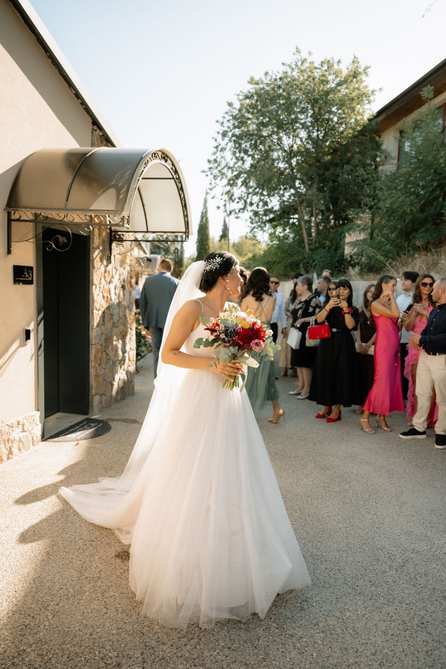 Wedding guests line a pathway to celebrate as a bride in a white ballgown dress walks past during an outdoor ceremony.