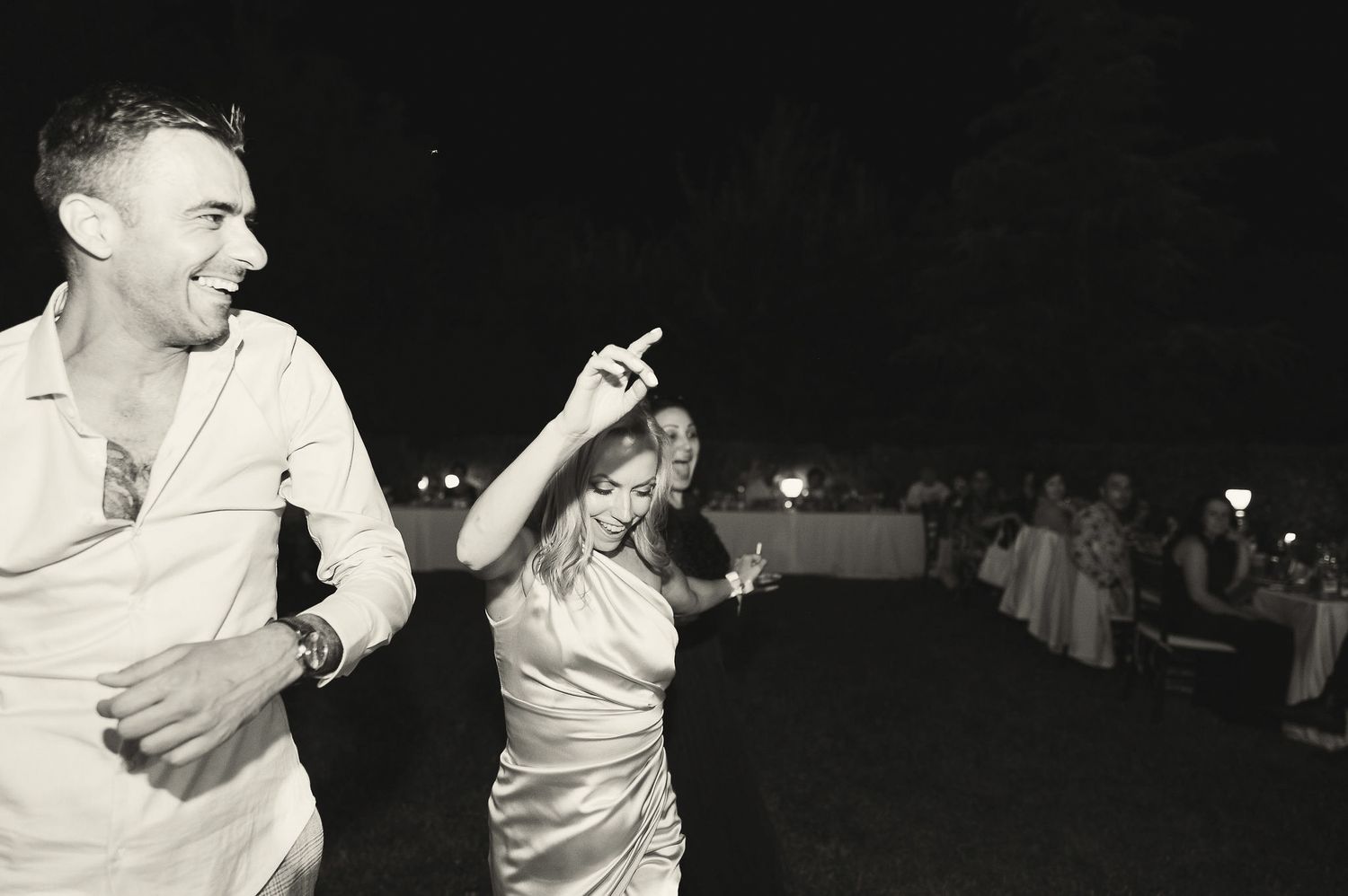 Black and white photo of guests dancing energetically at a nighttime celebration.