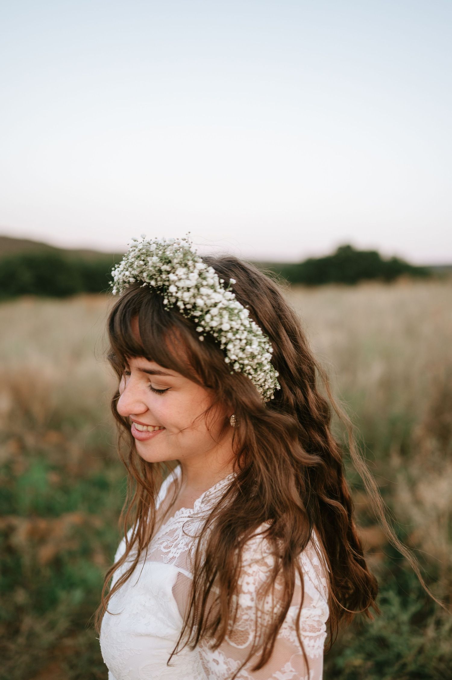 Side profile of bride with floral crown against sunset landscape.