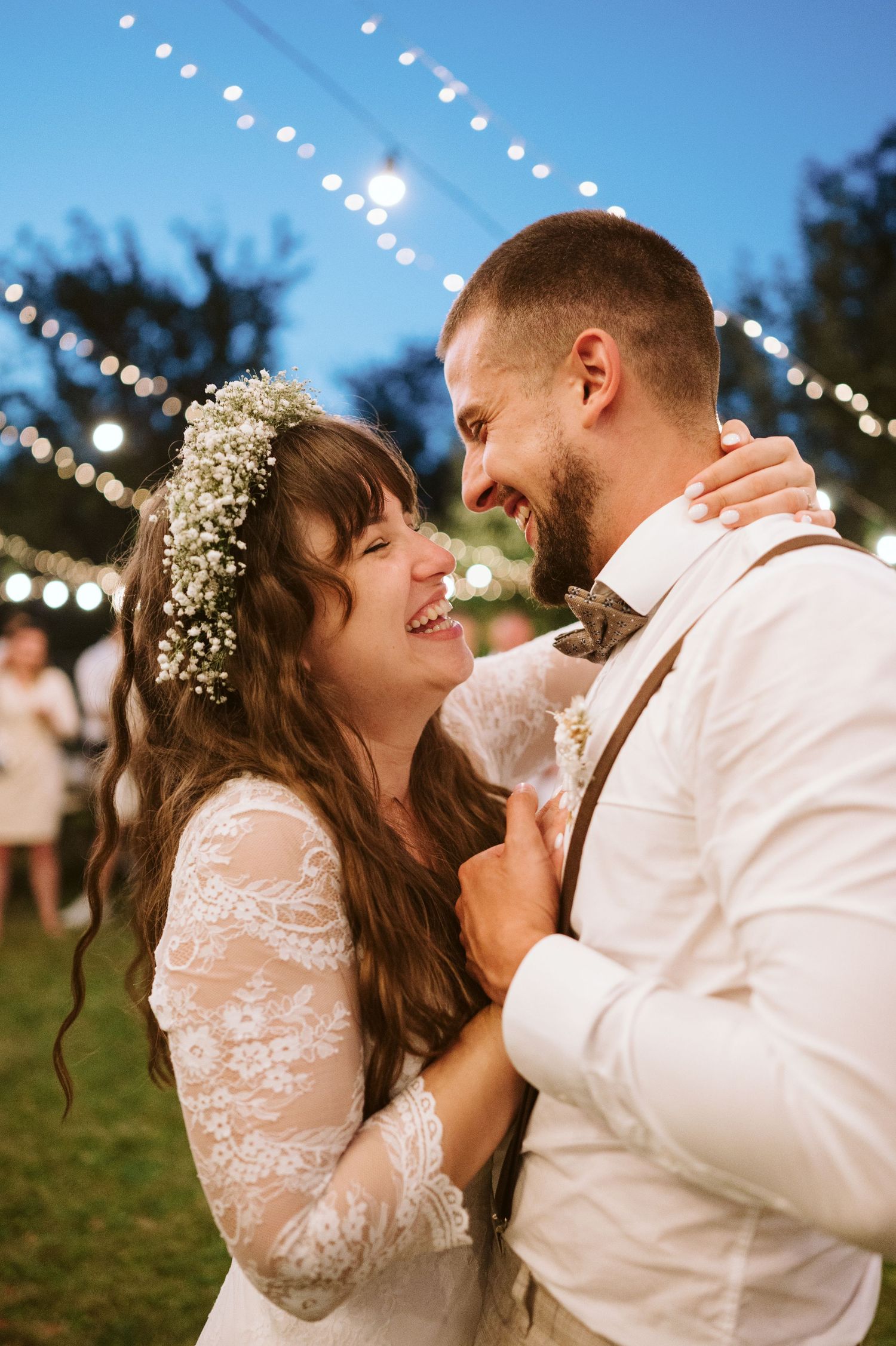 Intimate moment shared between newlyweds under twinkling string lights at dusk.