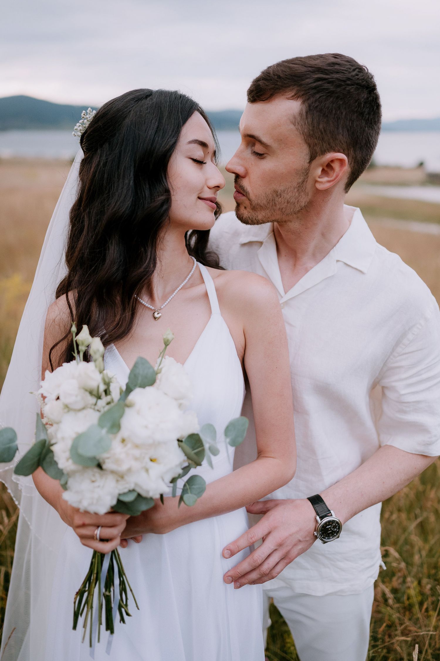 Intimate wedding portraits captured in natural meadow setting with white floral bouquet.