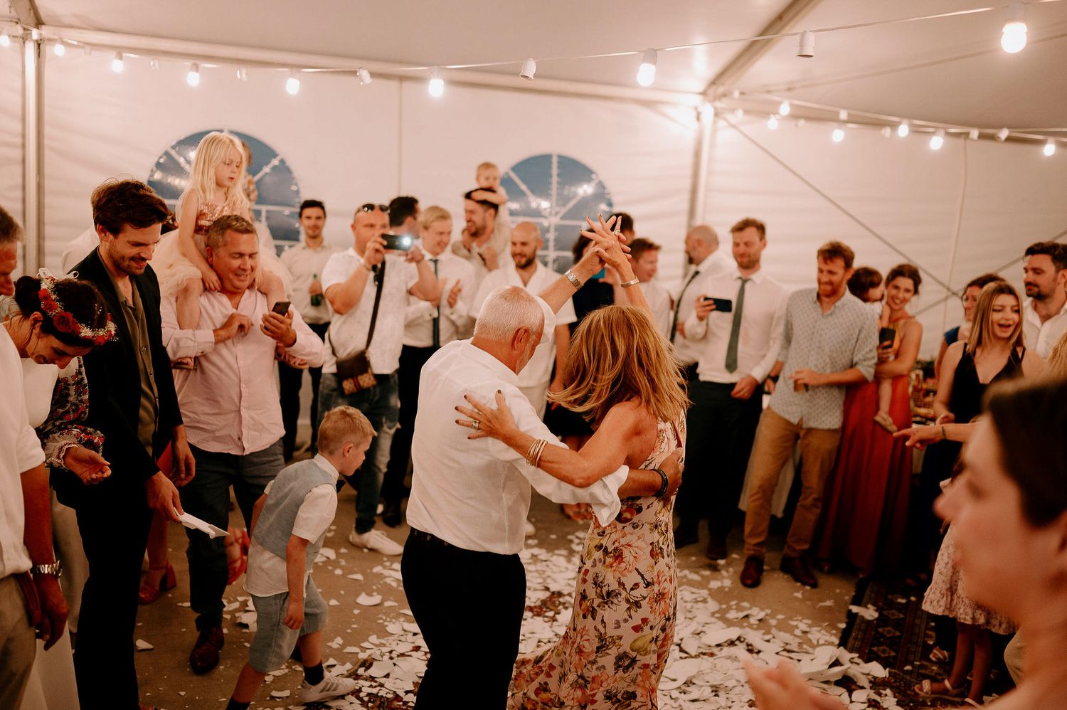 Joyful celebration with dancing and mingling at an evening wedding reception under string lights.