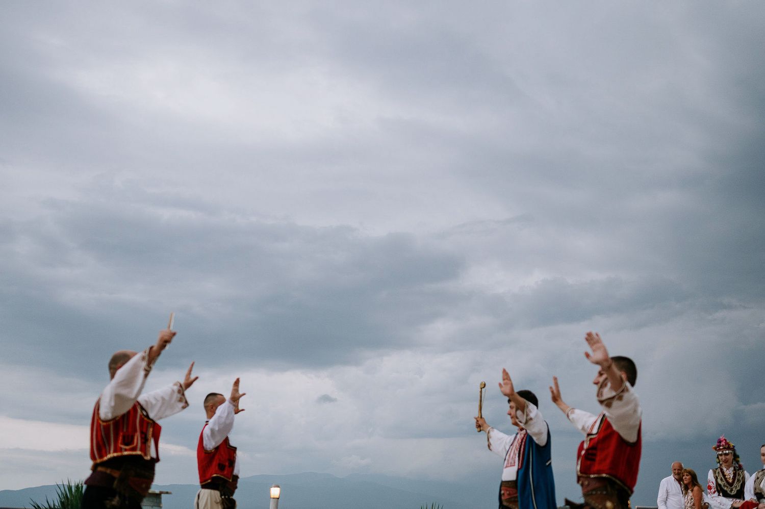 People raise their hands in celebration against a cloudy sky during an outdoor event.