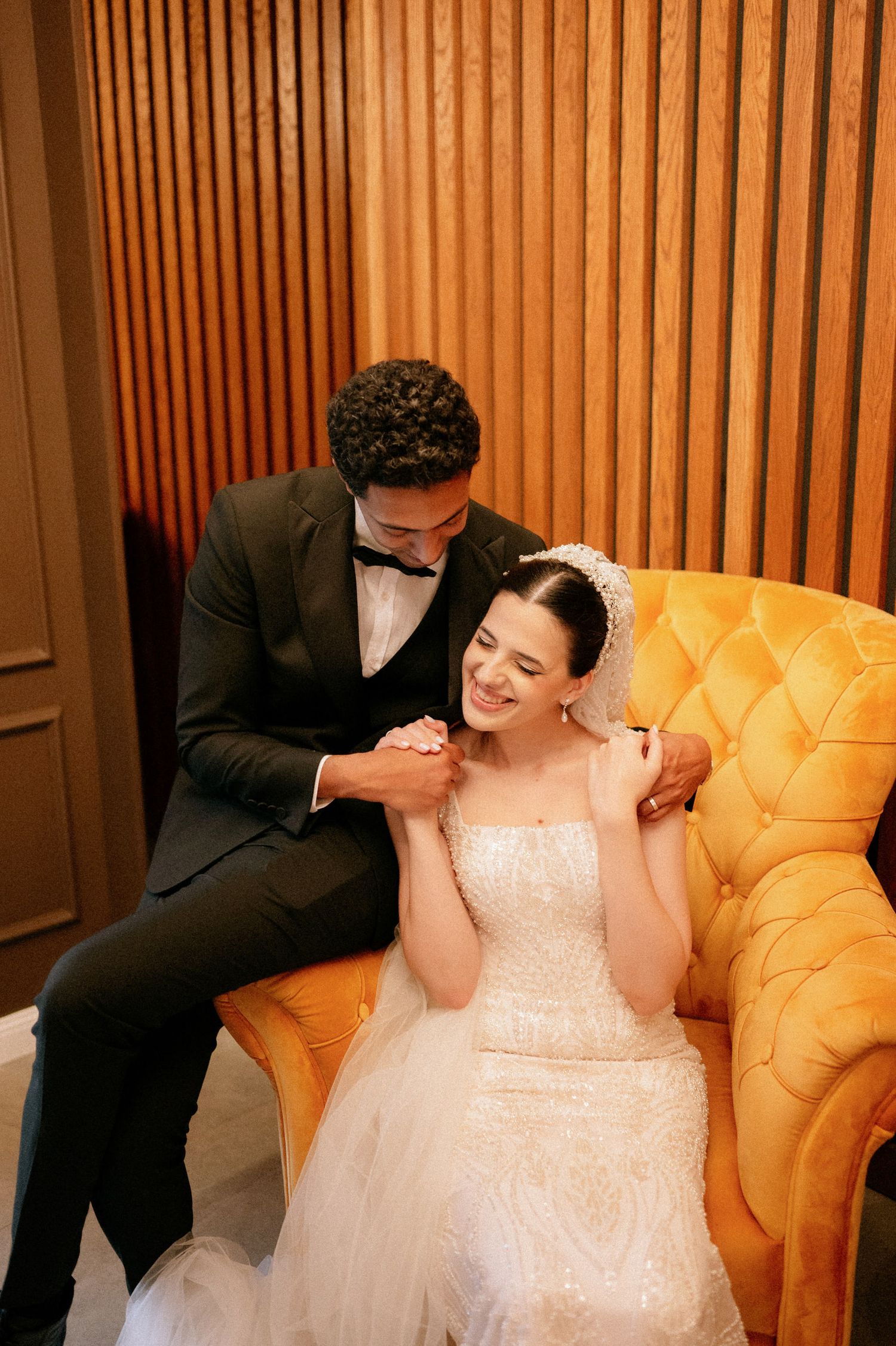 Intimate wedding photo session with a yellow tufted sofa against wooden wall panels.