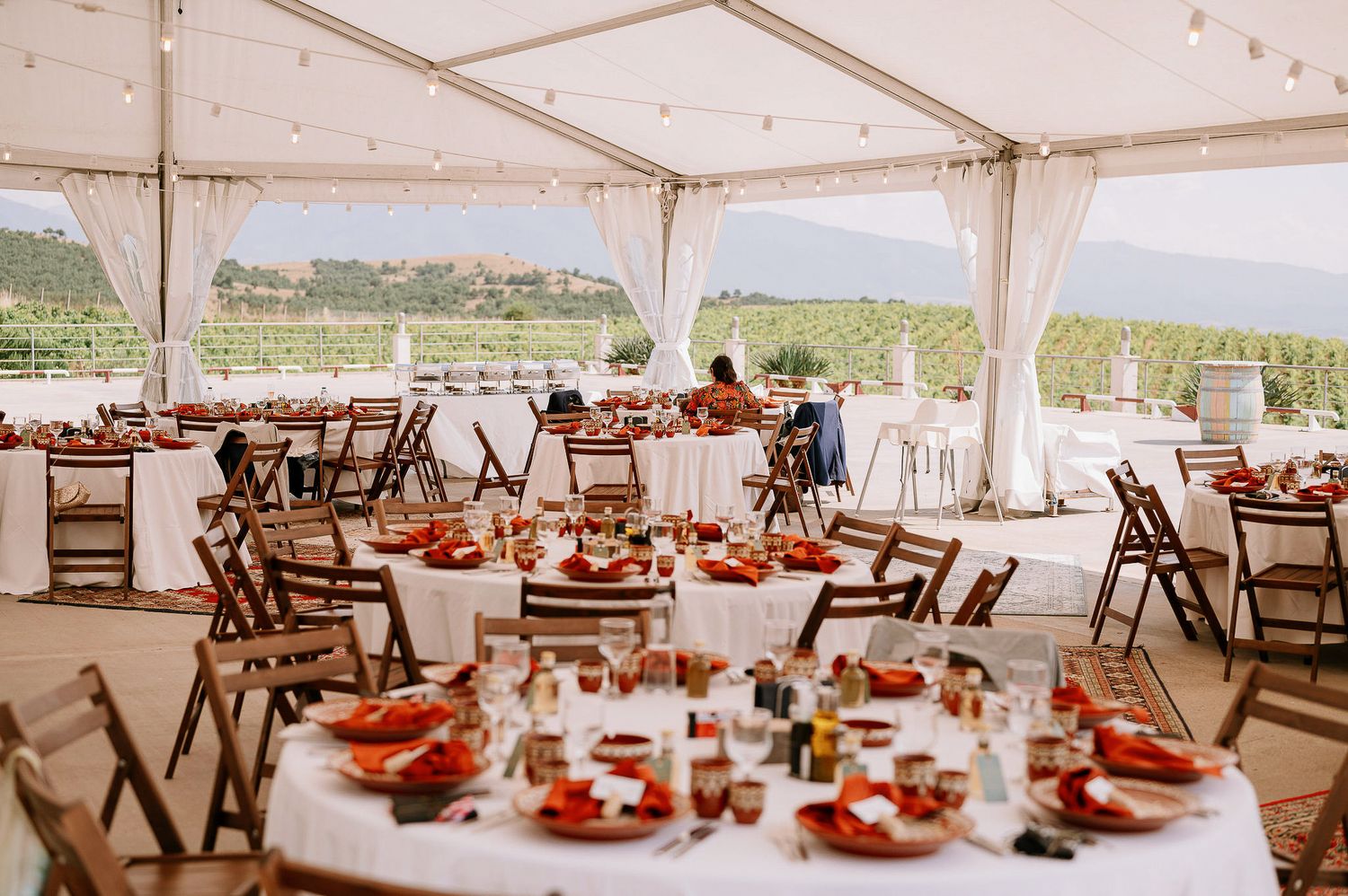 An elegant wedding reception tent with round tables set with coral accents and rustic wooden chairs.