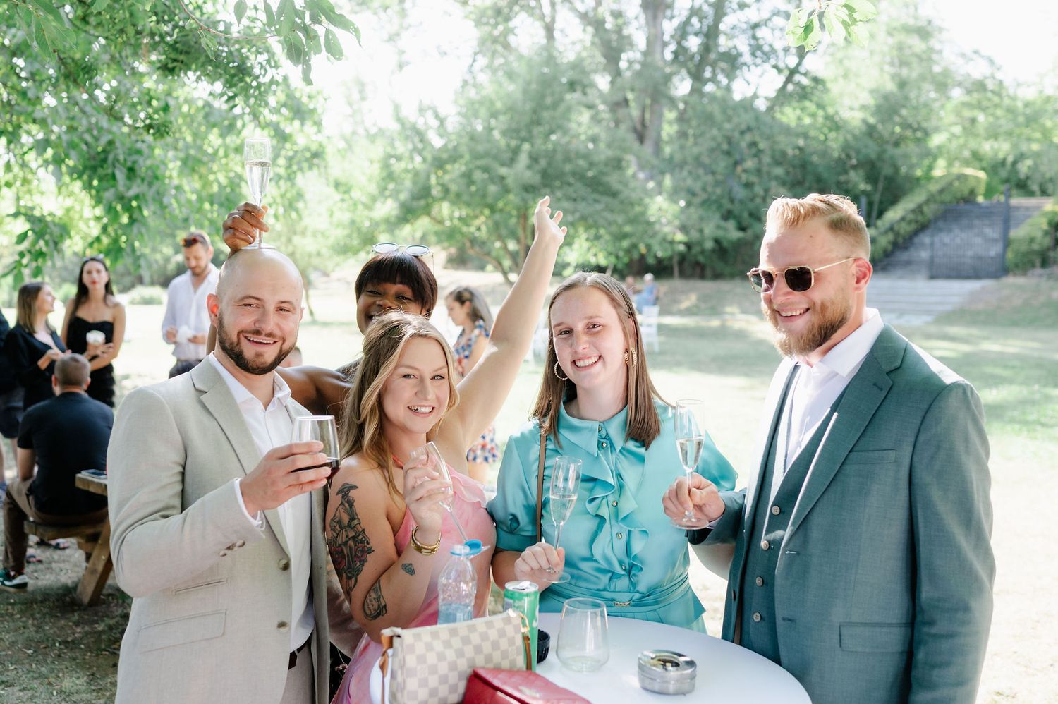 Guests socializing at an outdoor event under green tree canopy.