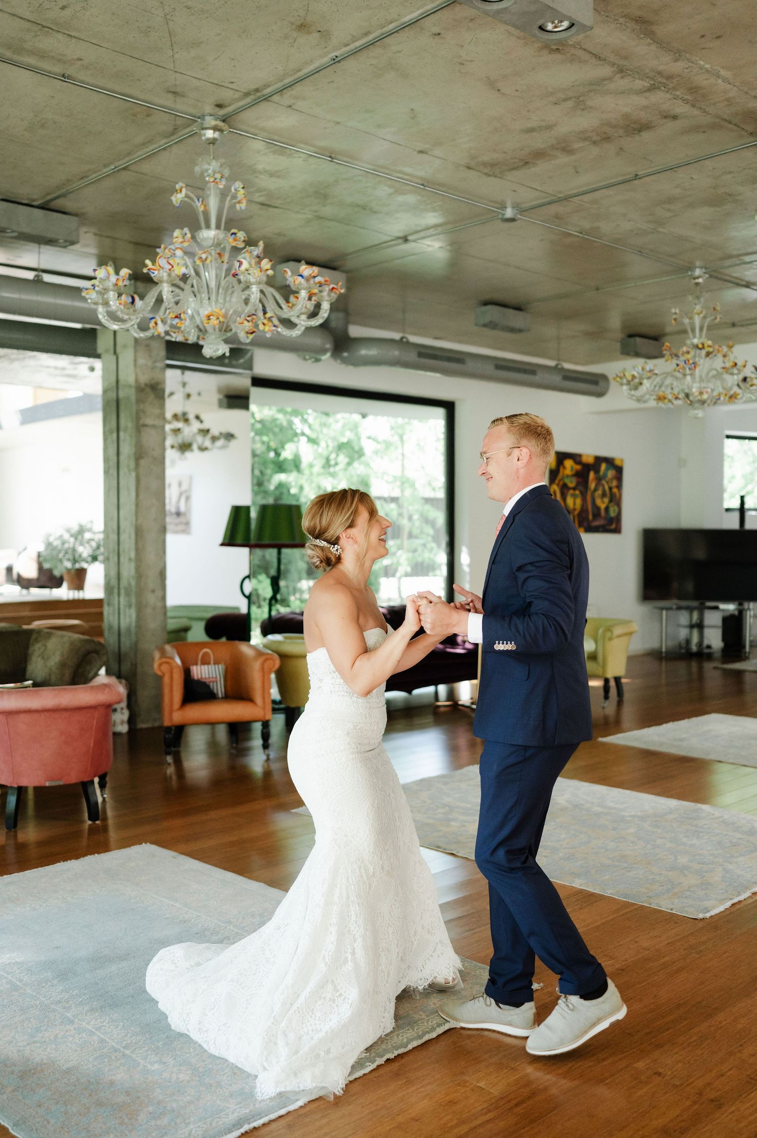 A wedding couple dances joyfully in a bright indoor venue with hardwood floors.