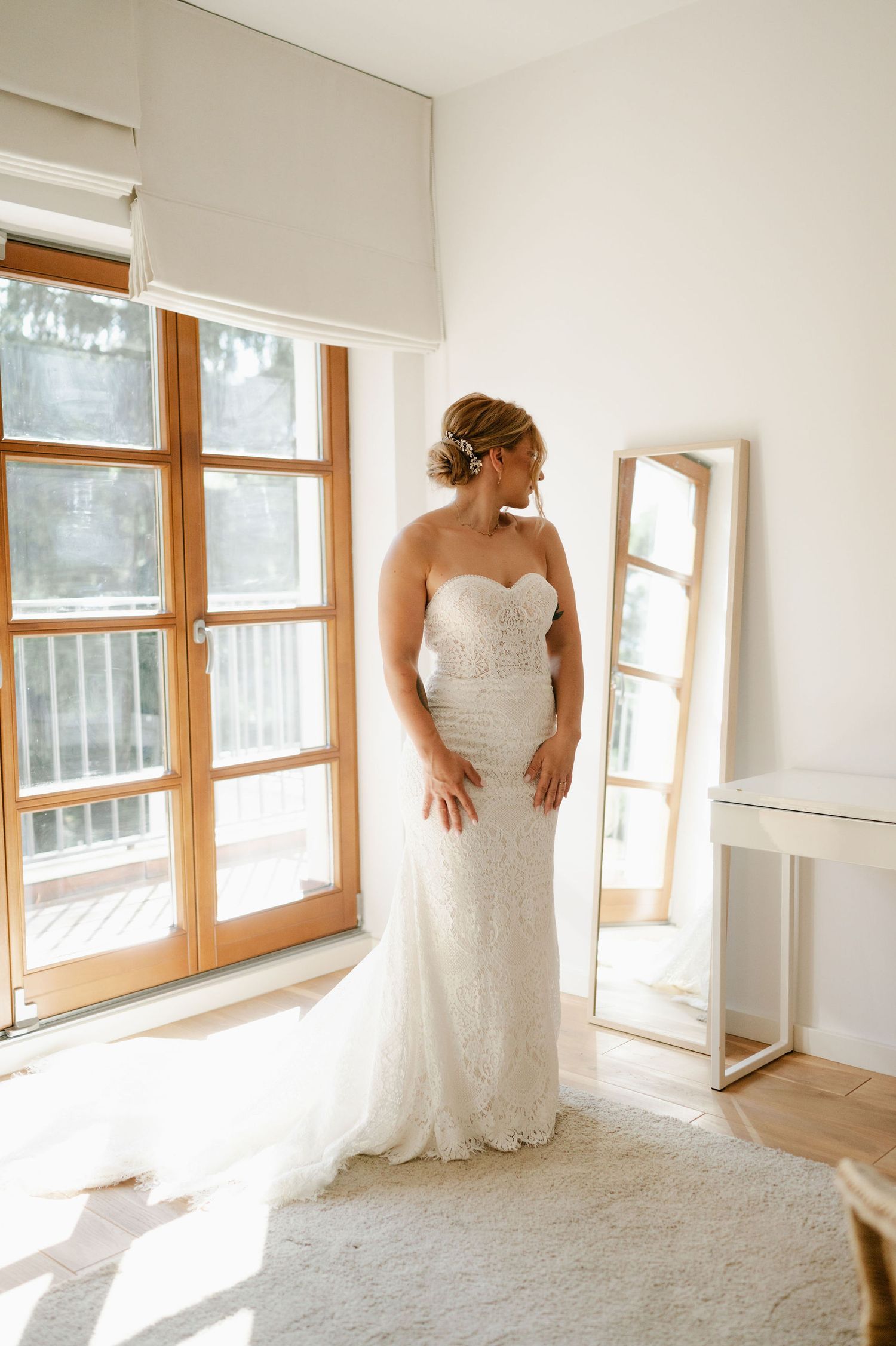 Sunlit bridal portrait by window in form-fitting lace wedding gown.
