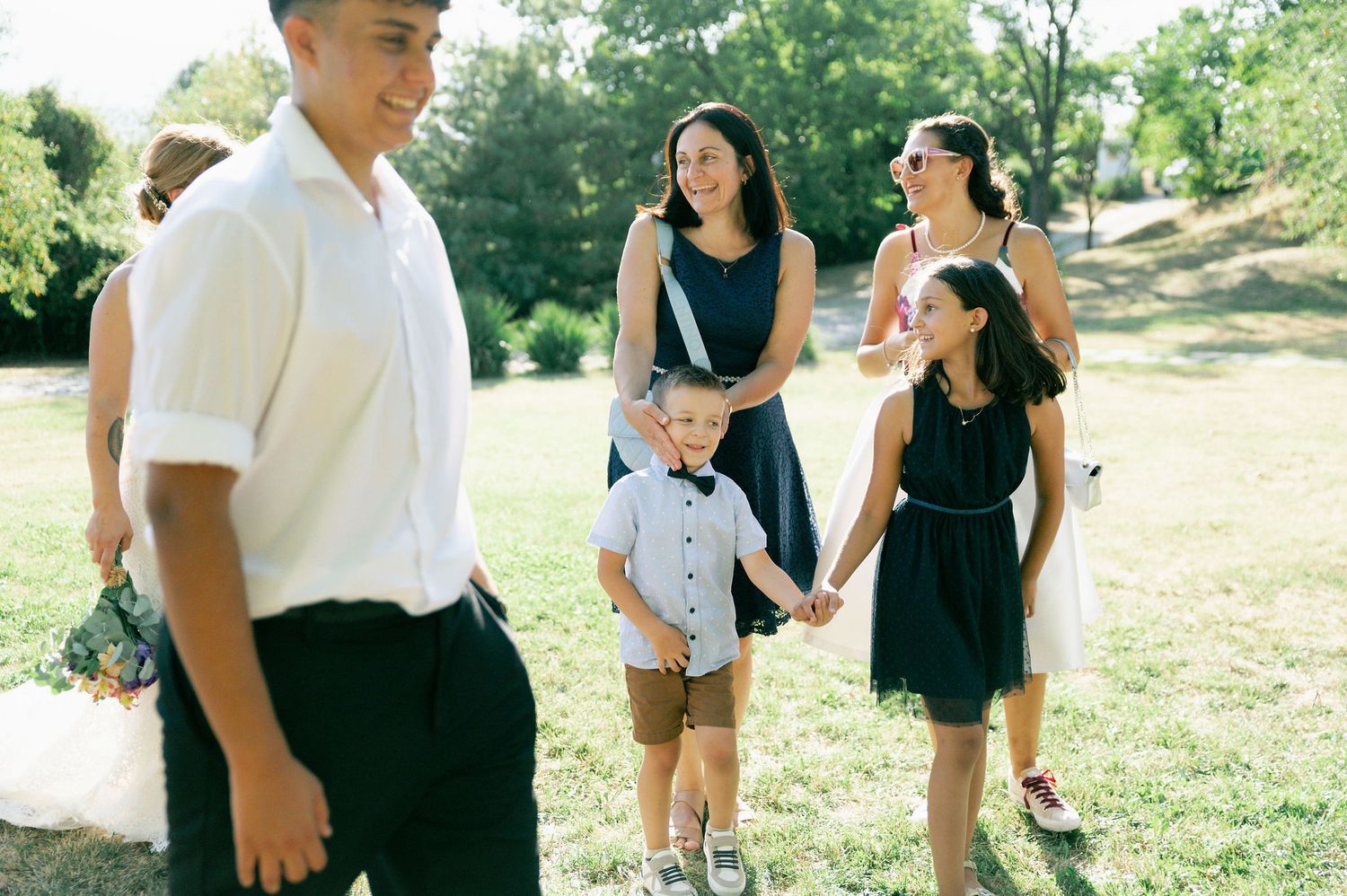 Wedding guests mingle and celebrate on a sunny hillside during an outdoor summer celebration.