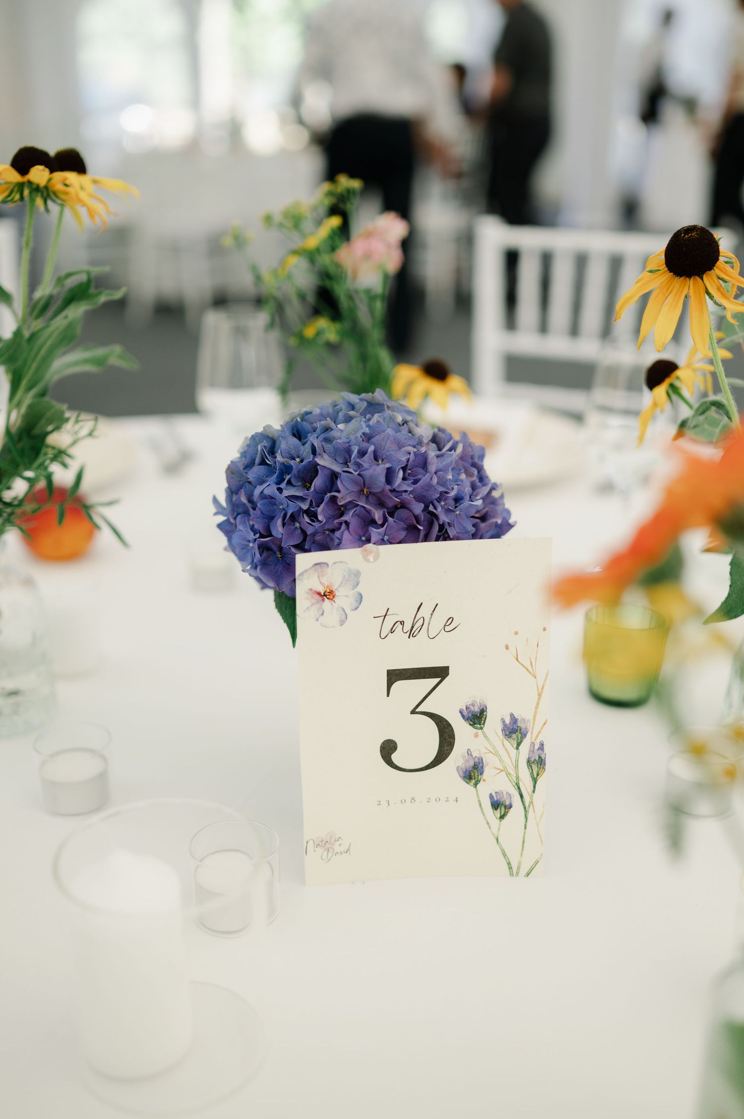 Watercolor table numbers with purple floral designs displayed among wedding reception decorations.