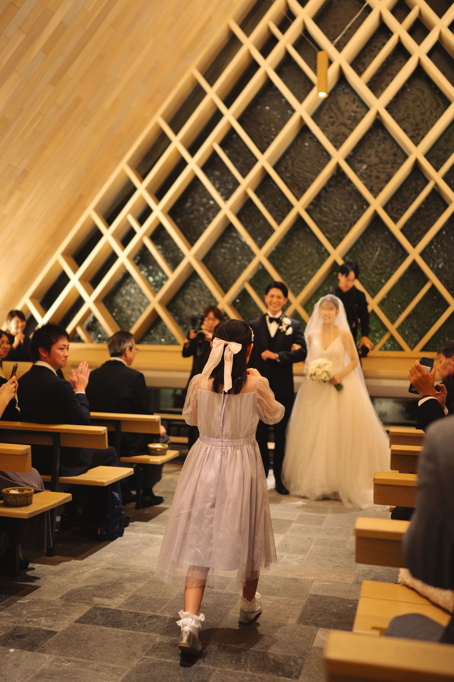 Wedding ceremony with flower girl walking past wooden benches and lattice walls.