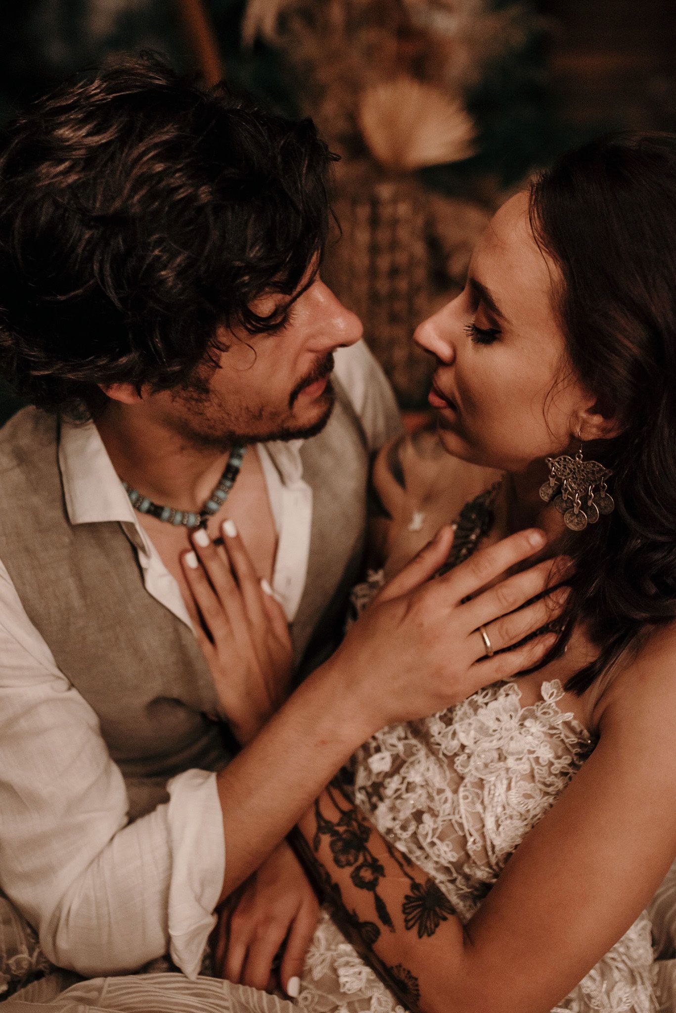 Romantic couple in intimate pose with bride wearing lace dress and groom in vest during moody wedding photoshoot.