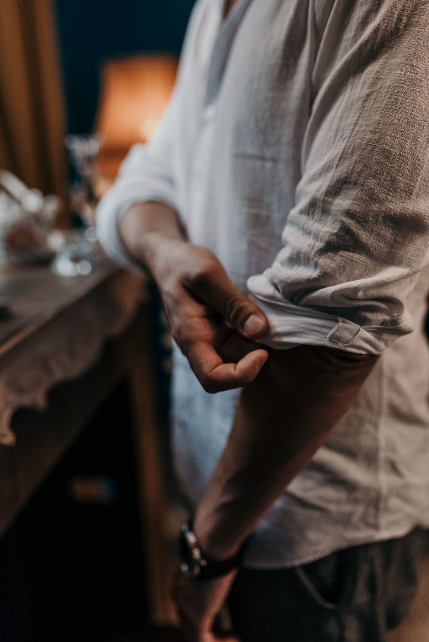 Close-up of hands rolling up white shirt sleeve against wooden furniture.