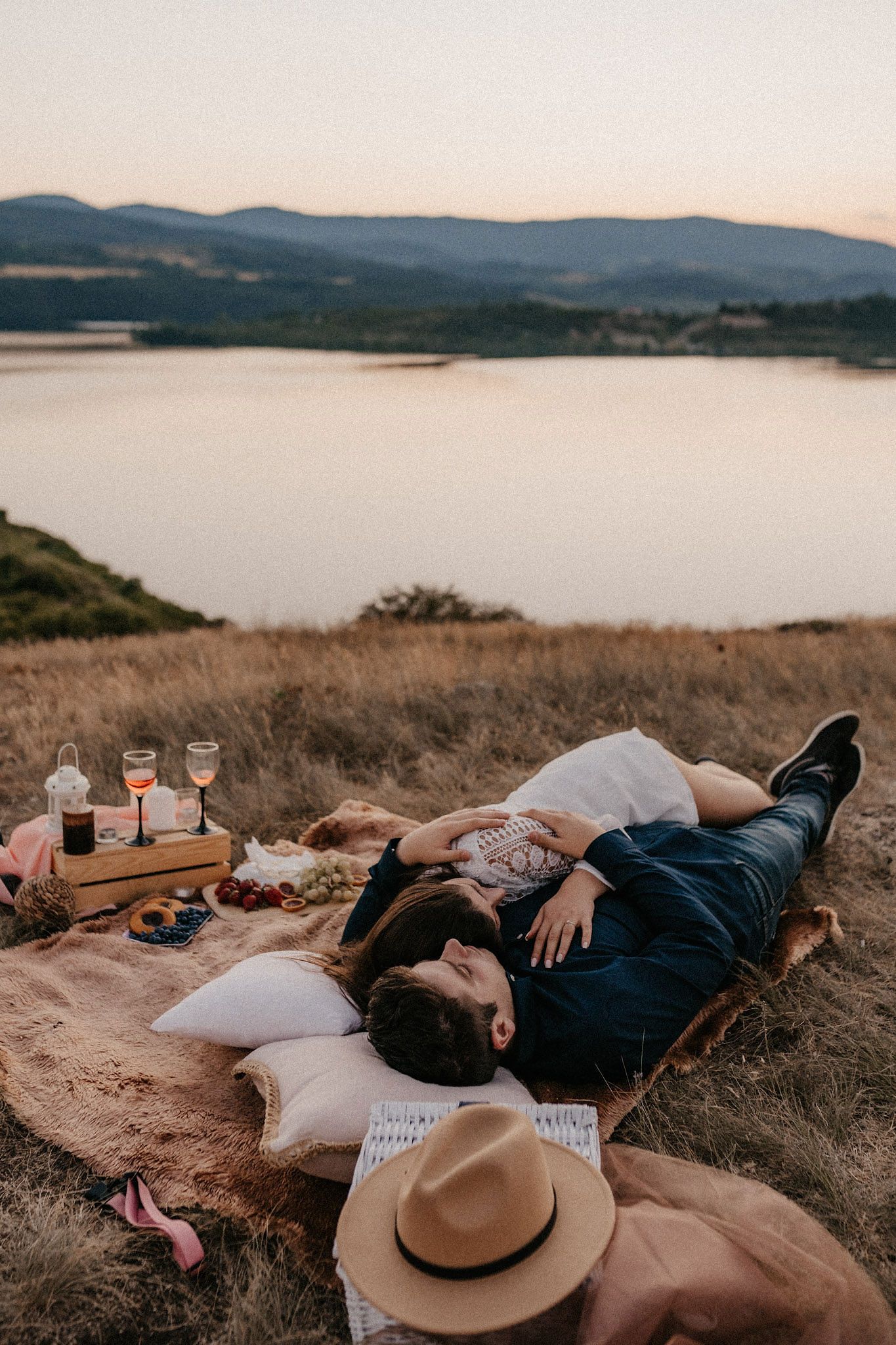 Panoramic view of lake and mountains with couple relaxing on picnic blanket.