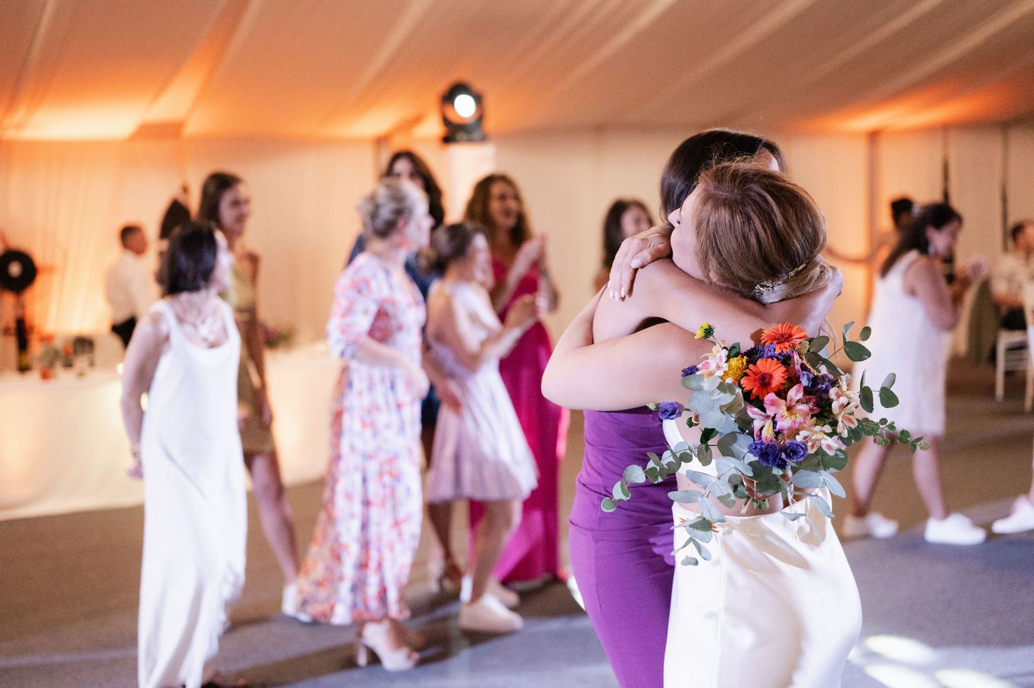 Wedding guests dancing together in a reception hall with warm lighting and festive atmosphere.