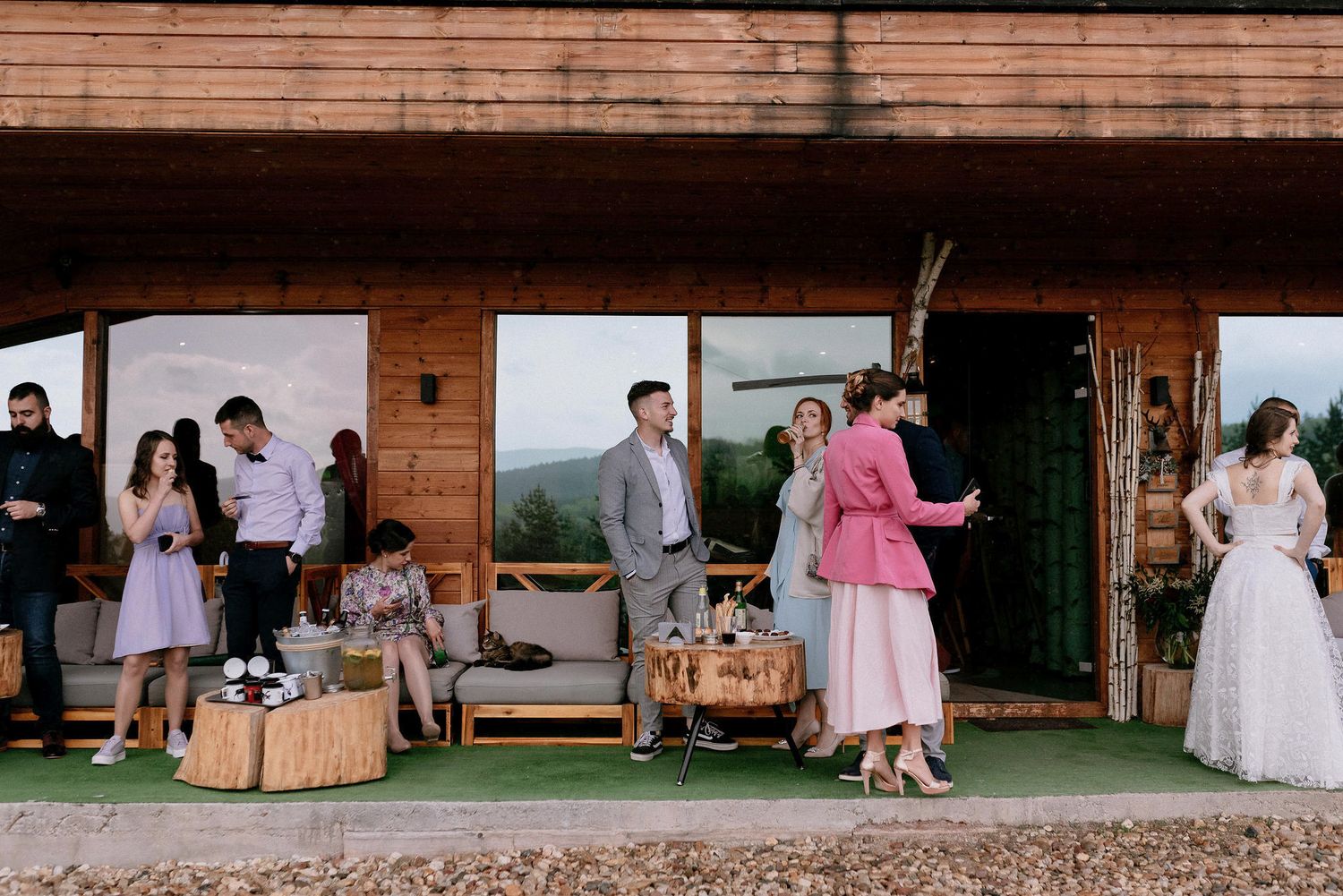 Wedding celebration at a rustic wooden venue with guests mingling on a covered porch.