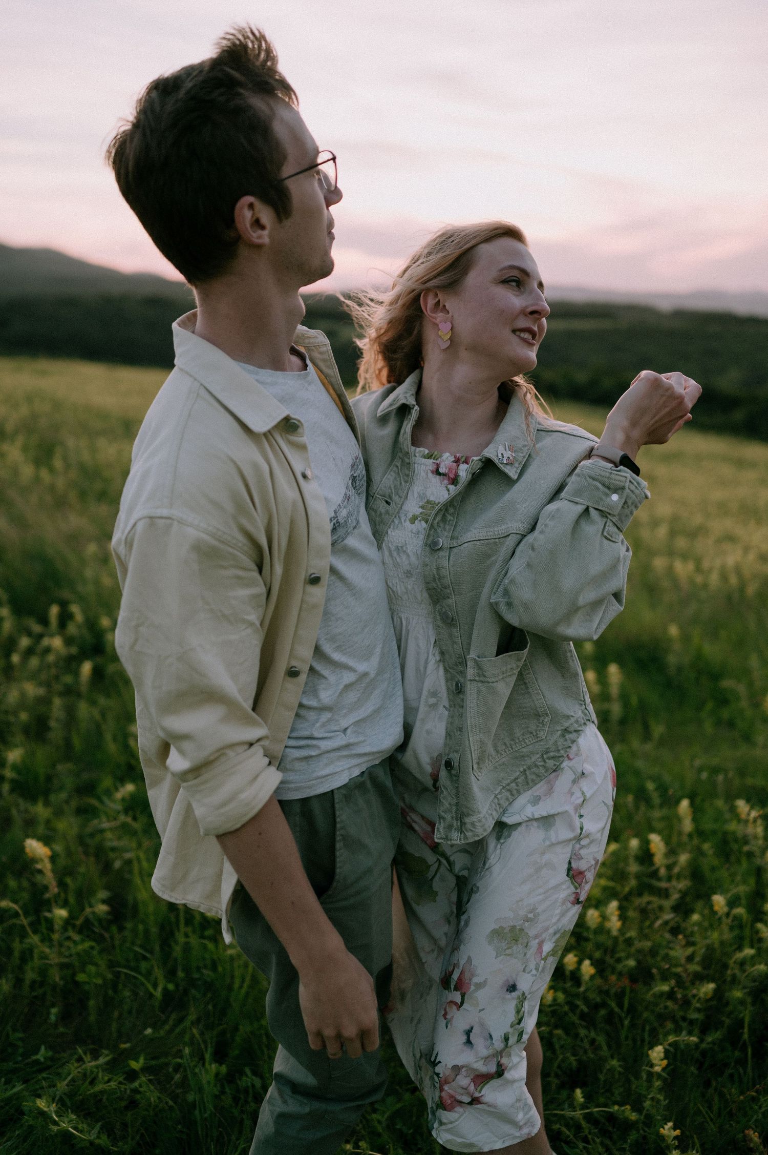 Two people share a joyful moment while dancing in a field of yellow wildflowers at dusk.
