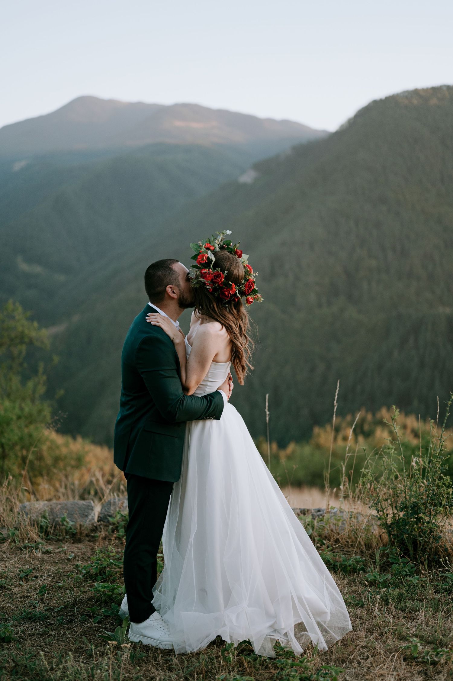 A newlywed couple embraces on a mountainside during their outdoor wedding photoshoot.