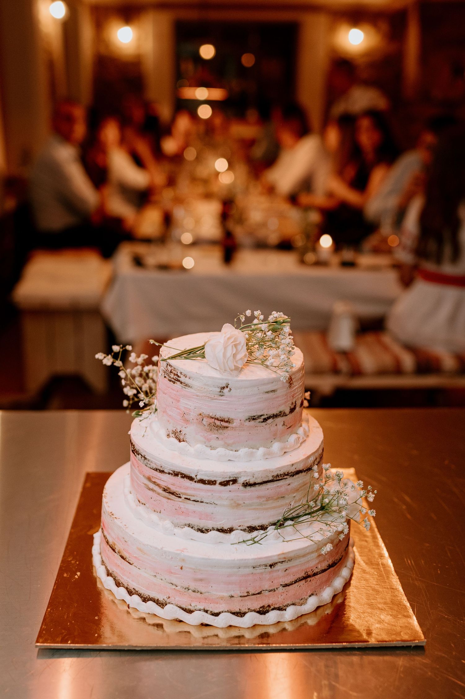 Three-tiered white wedding cake with delicate floral decorations on a gold base.