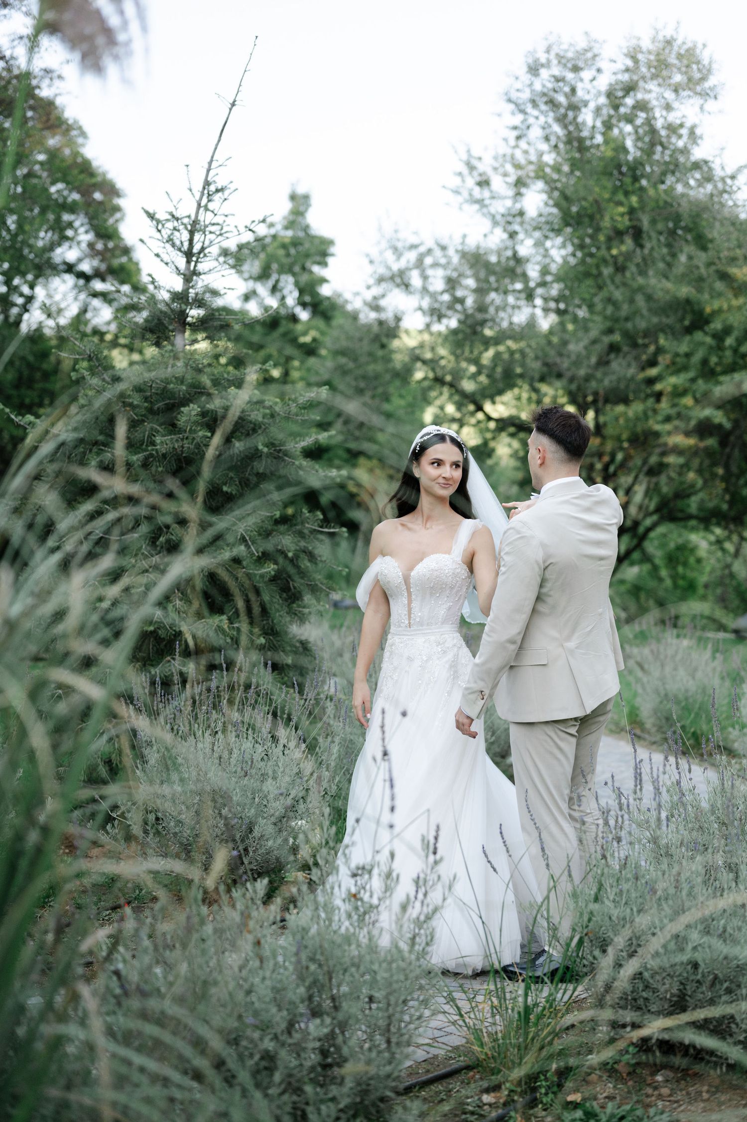 Wedding couple walks through garden path surrounded by wild lavender and greenery.