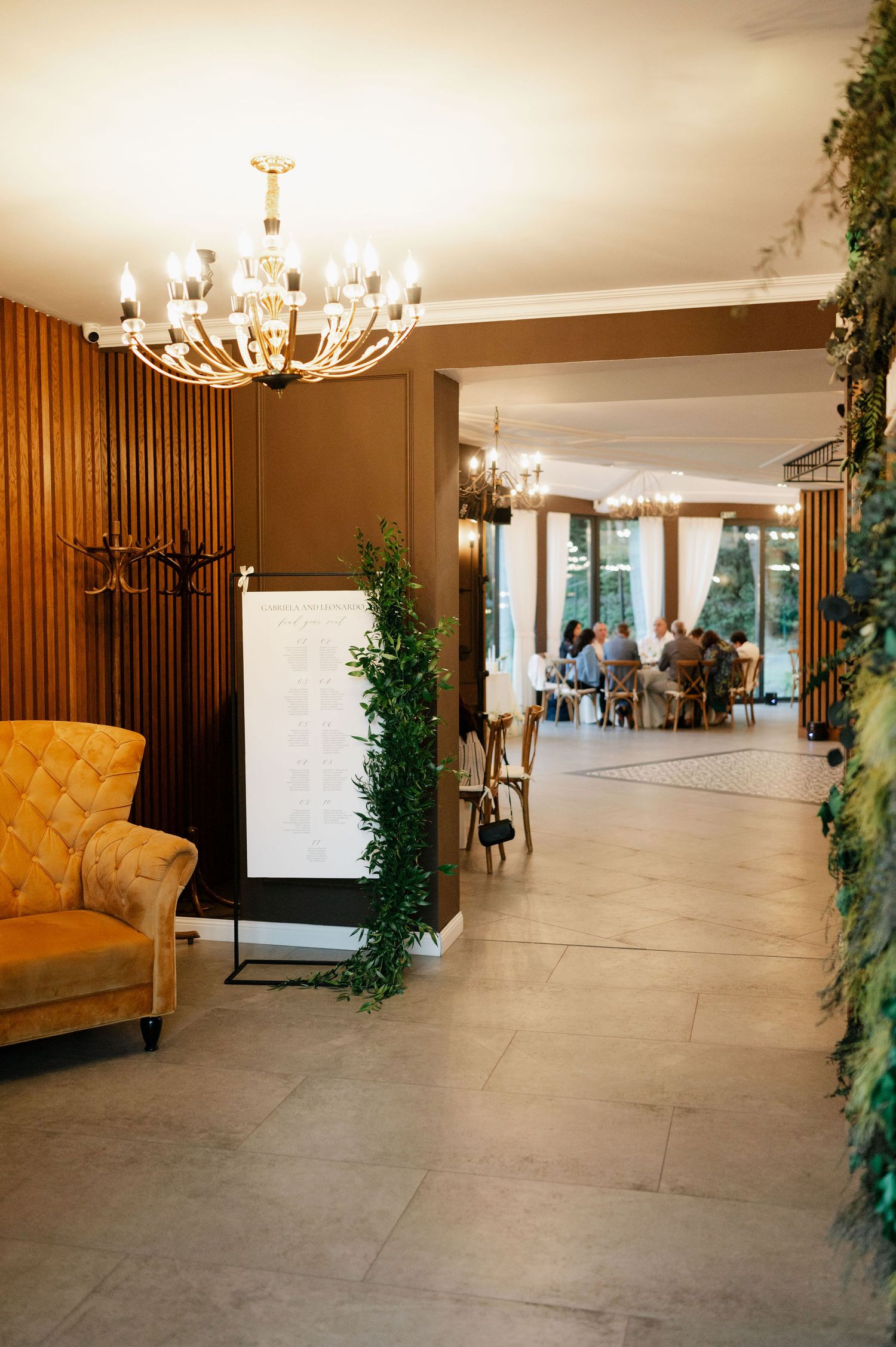 Modern event venue interior with yellow accent chairs, chandeliers, and wood panel walls.