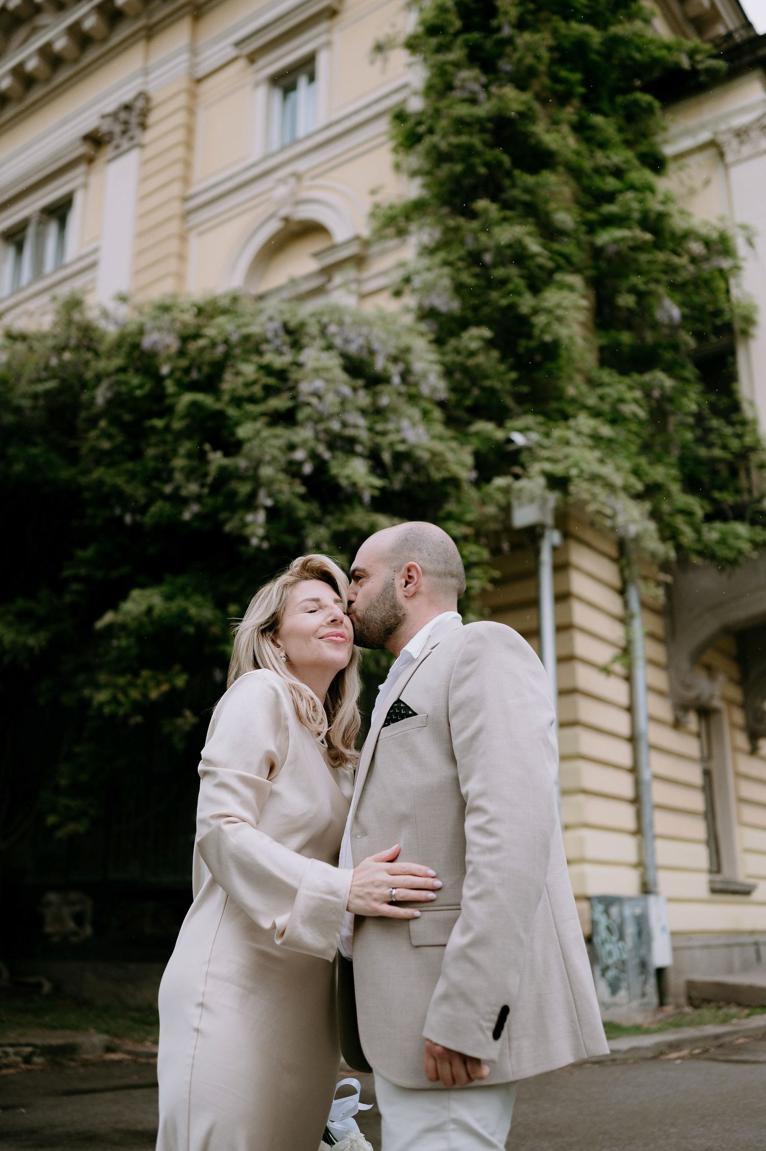 Intimate moments between couple in matching cream outfits by historic facade.