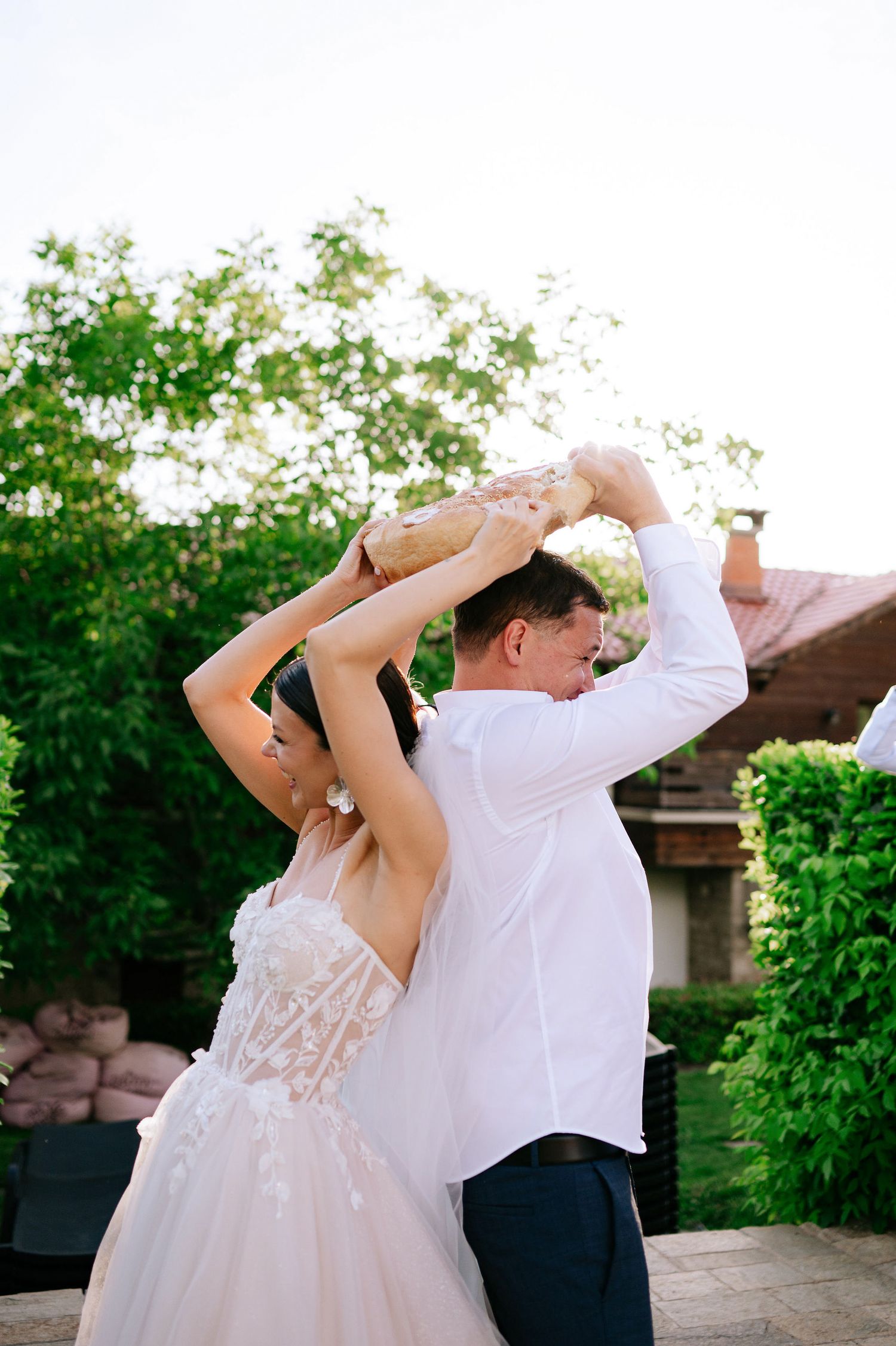 A couple in wedding attire performs a playful dance move on an outdoor patio during sunset.