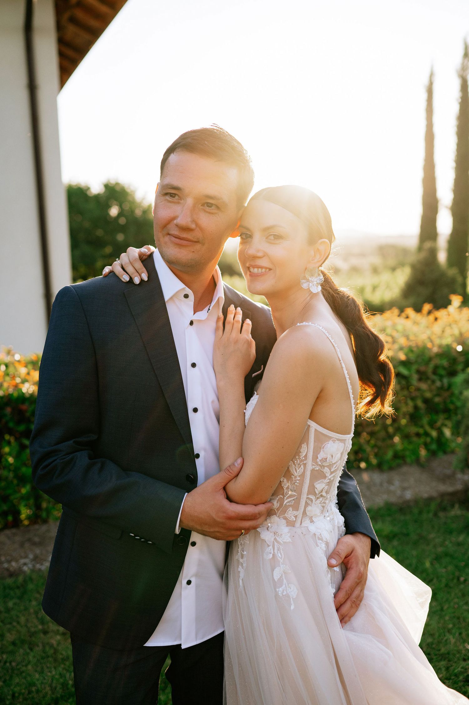 A romantic wedding photoshoot in a garden at golden hour with a couple embracing in formal attire.