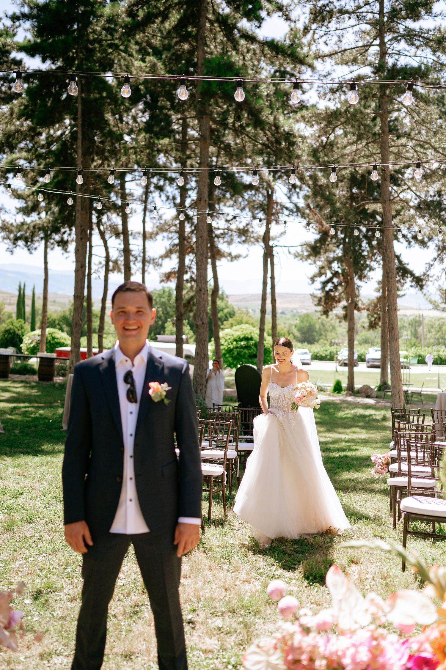 Sunlit outdoor wedding ceremony space with wooden chairs and floral decorations.