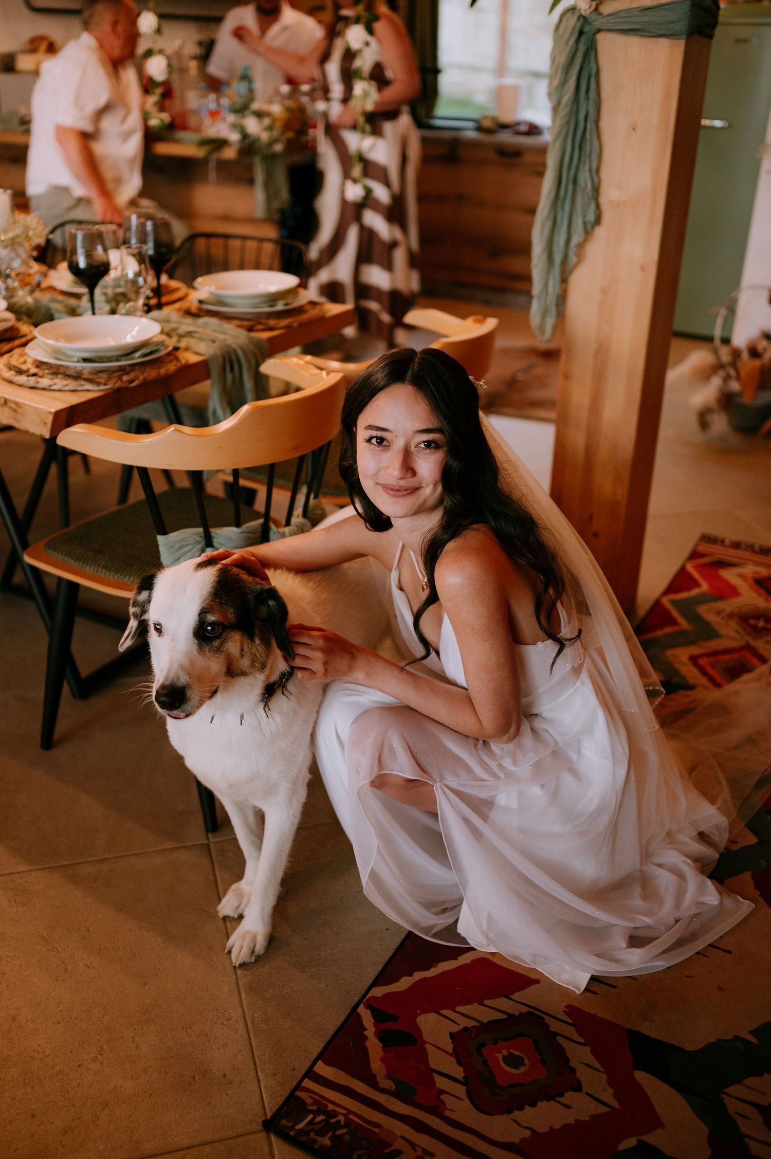 A person in a white dress kneels beside a spotted dog on a patterned rug at an indoor event.