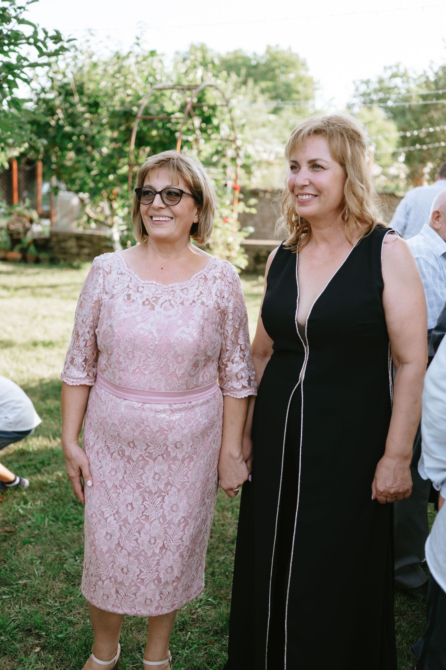 Wedding guests in pink and black dresses smiling together at an outdoor celebration.