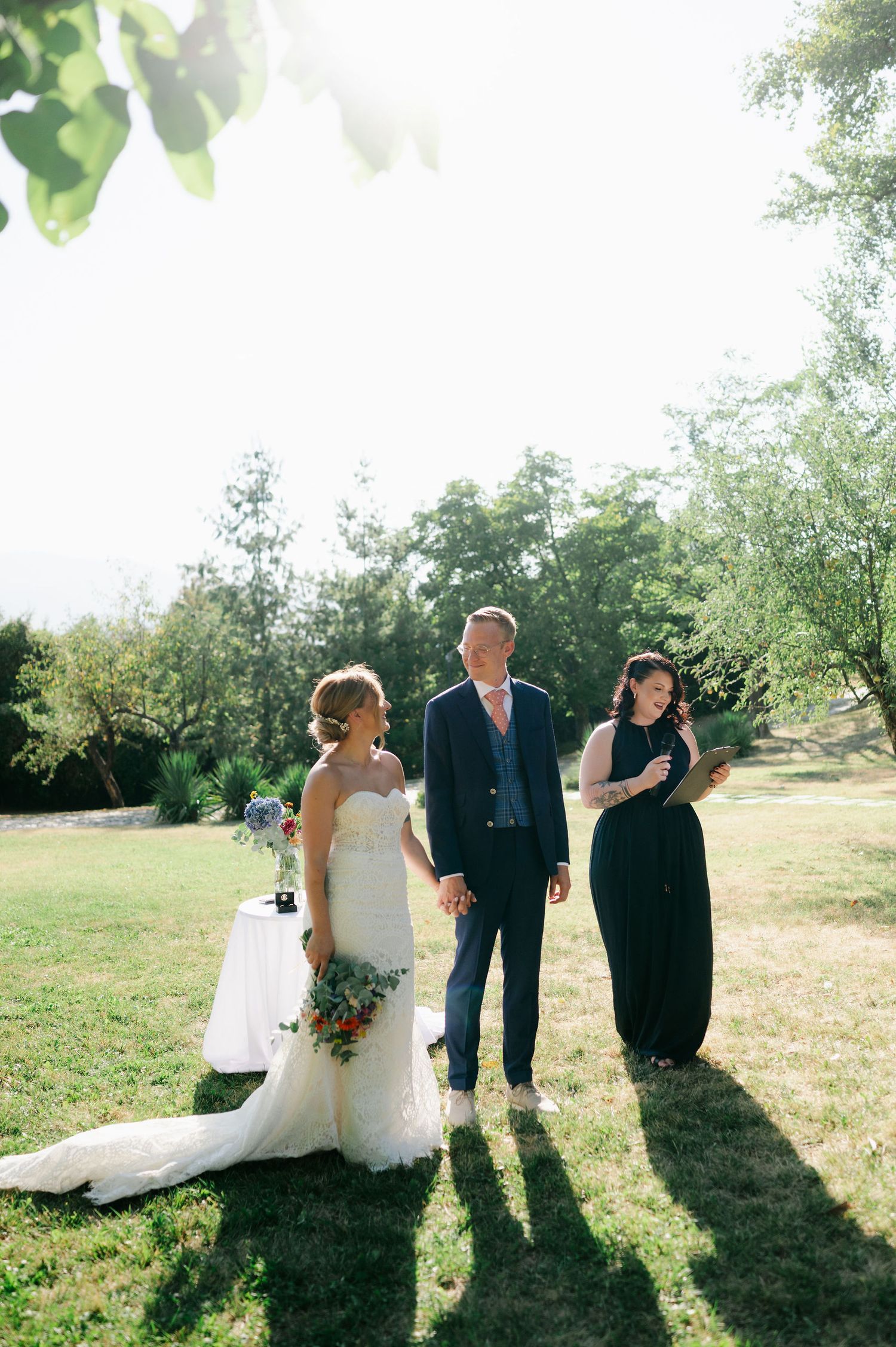 An outdoor wedding ceremony unfolds on a grassy field with beautiful natural lighting and shadows.